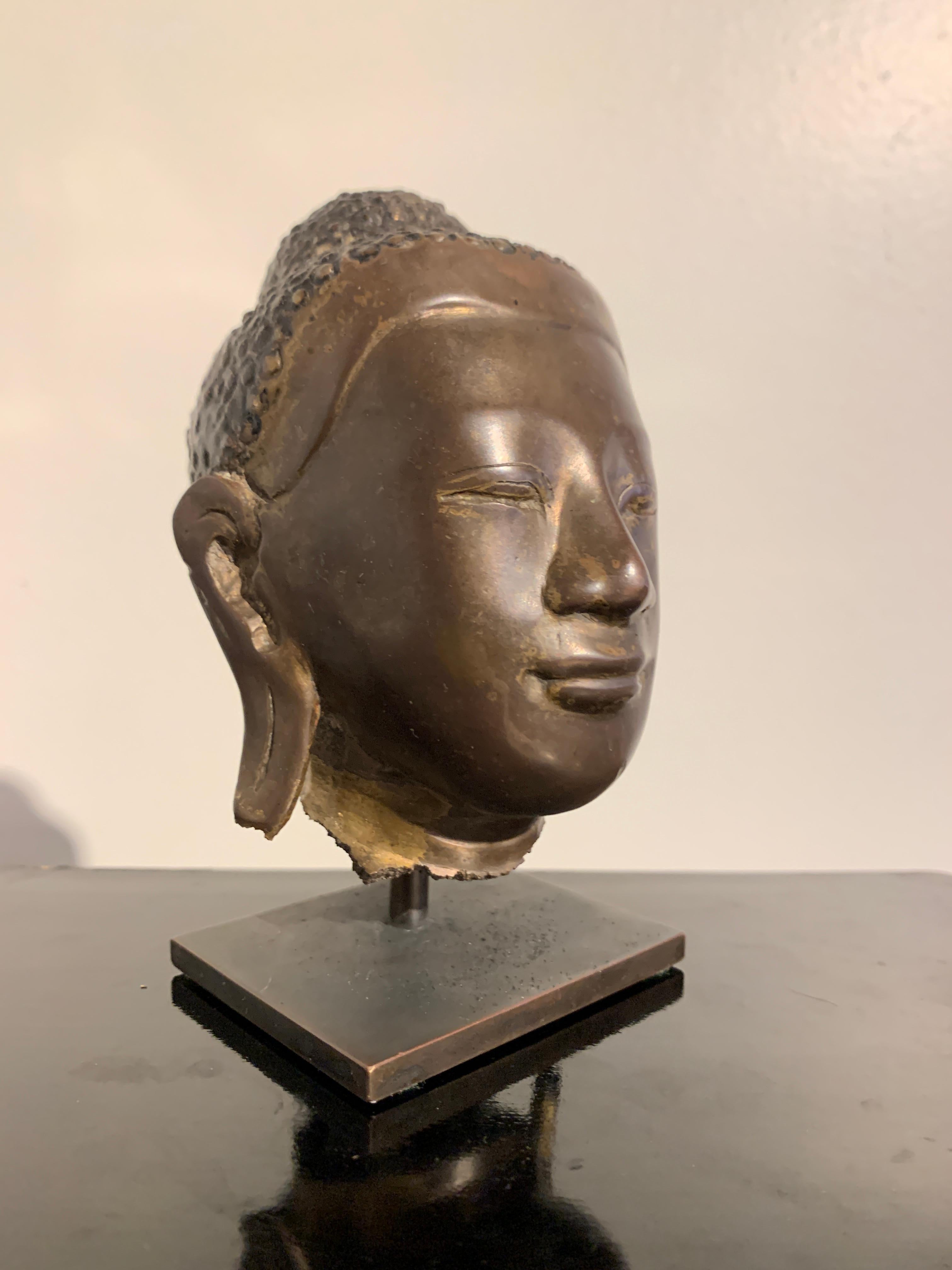 A charming Burmese Mandalay style bronze Buddha head, Mandalay period, mid to late 19th century, Burma.

The bronze head originally part of a larger statue, and broken at the neck. The Buddha's face sweet, and typical of the Mandalay style, with a