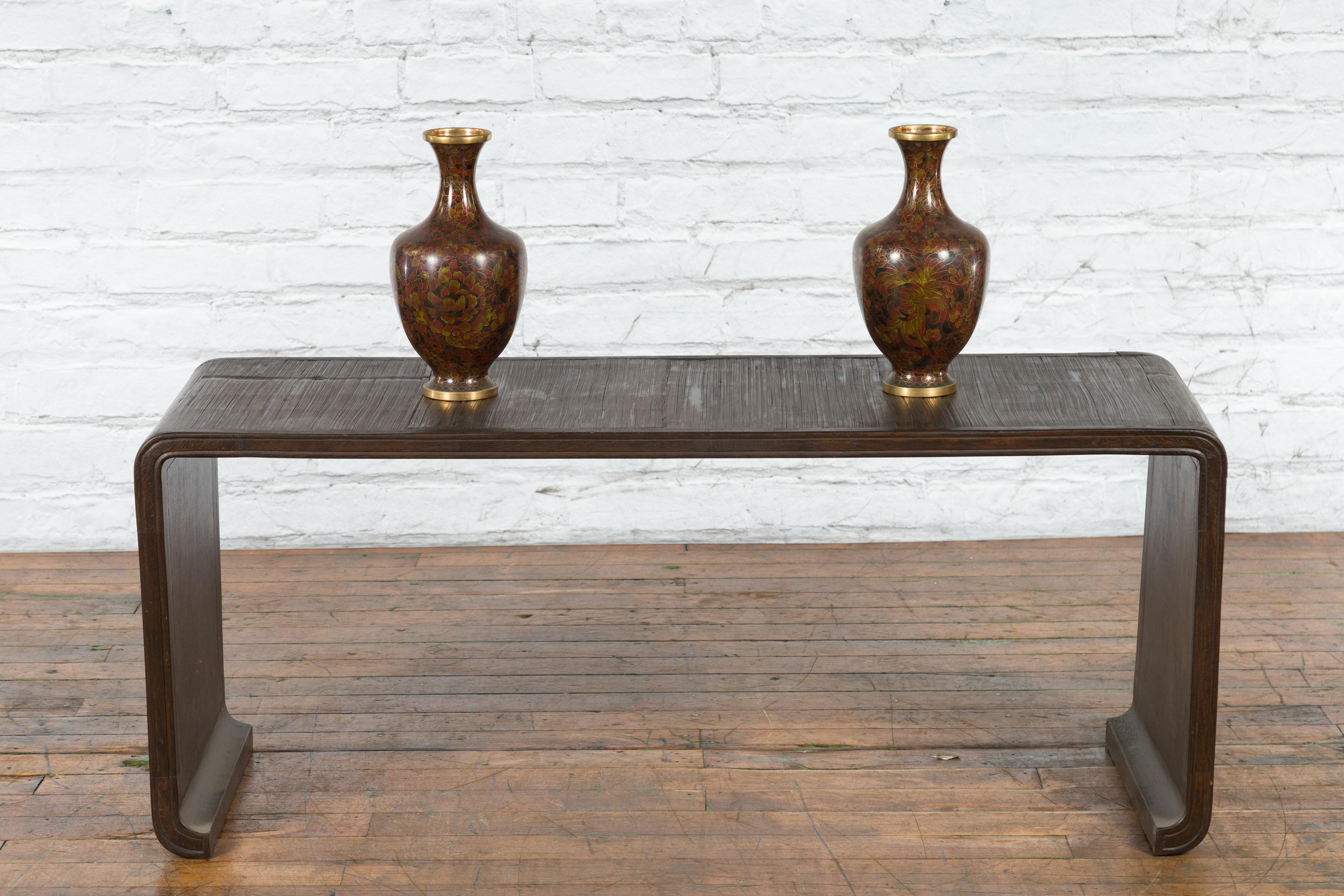 A vintage Burmese waterfall wooden coffee table from the mid-20th century with bamboo opium mat top, scrolling extremities and dark patina. Created in Burma during the midcentury period, this waterfall coffee table features a rectangular bamboo