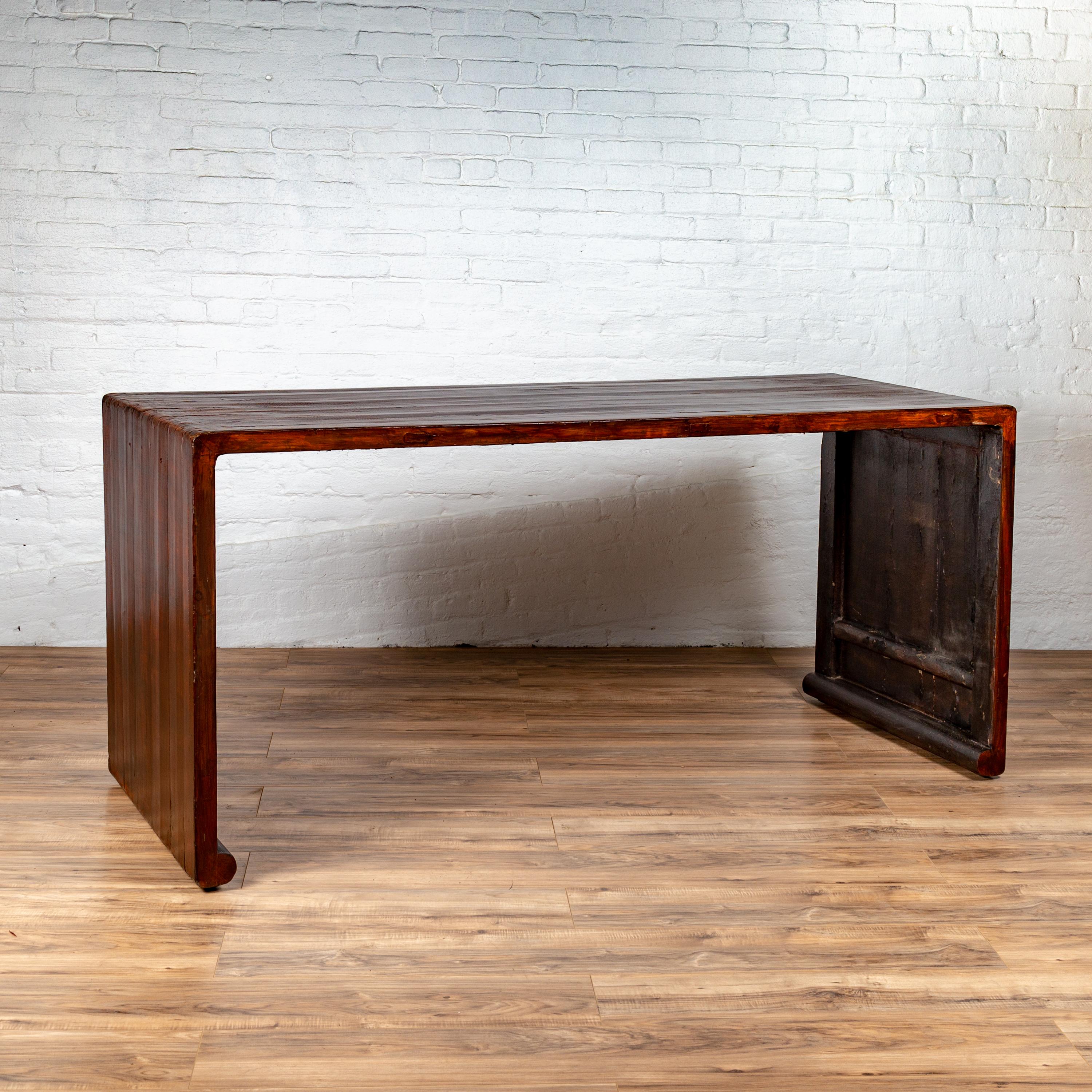 A vintage Burmese waterfall console table from the mid-20th century, with scrolling feet and dark patina. Born in Burma during the mid-century period, this elegant console table features a waterfall wooden frame with solid boards, boasting a lovely