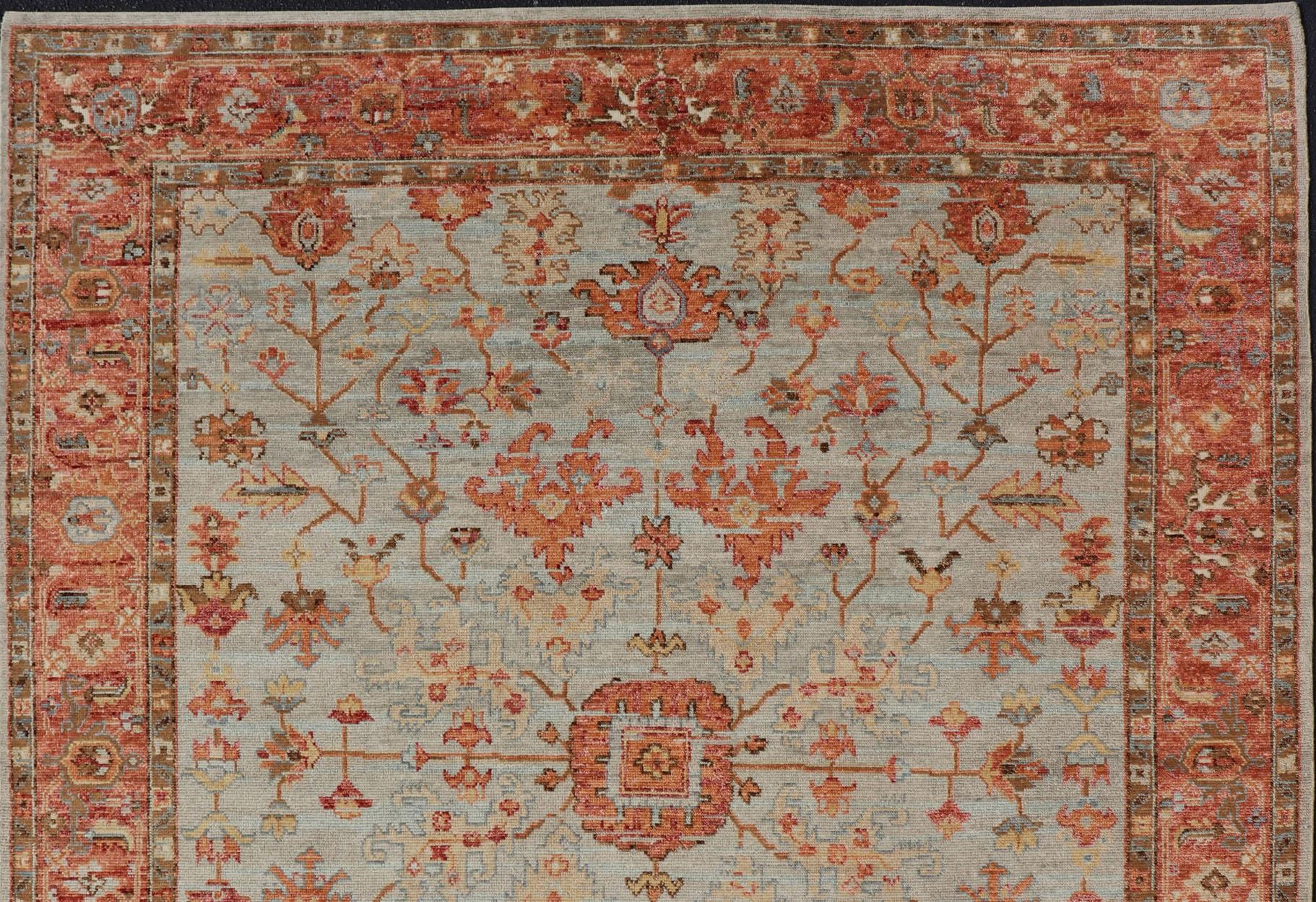 Measures 8'0 x 9'10 

This modern Indian Oushak was hand-knotted during the 2020's. The cool blue-gray field is heavily decorated in floral and leaflet motifs, commonly seen with Oushak carpets. The design is rendered in a fiery burnt orange with