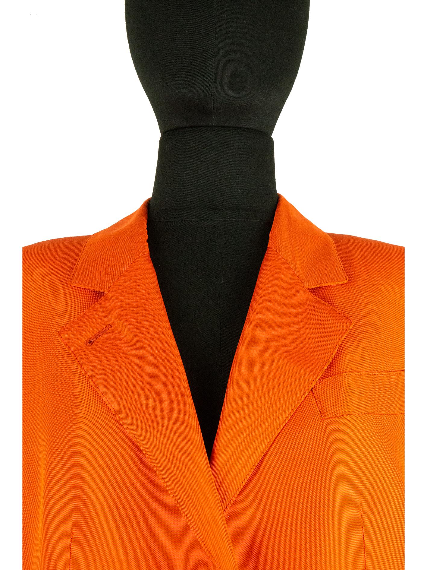 A burnt orange Hermès single-breasted blazer. This long single-breasted blazer features a notched lapel with a decorative buttonhole on the right side. Just below the lapel are three gold-coloured buttons in the shape of two-piece of bamboo. At the