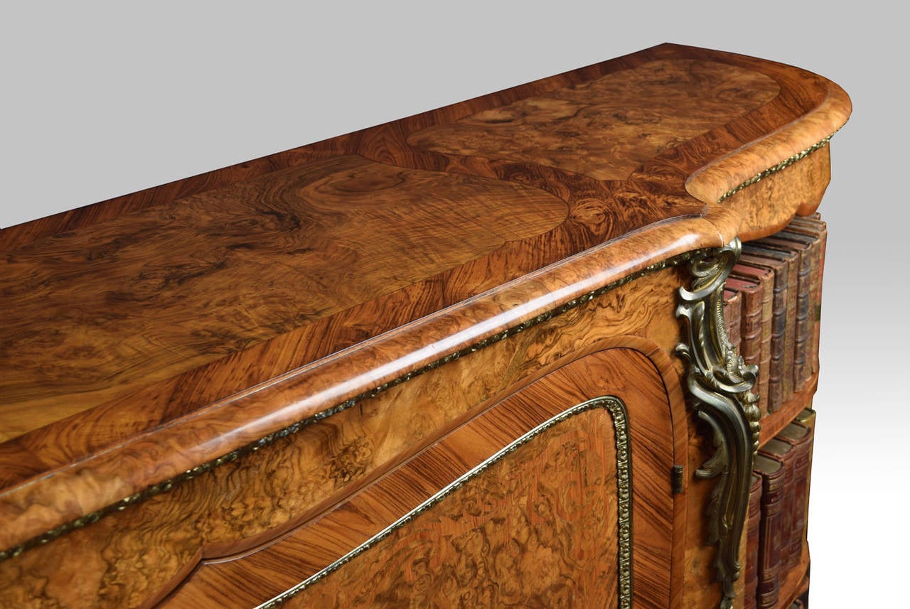 Burr walnut and tulipwood ormolu-mounted credenza, the rectangular top having bowed ends with unusual crossbanded top above two central doors inlaid with ribbons and scrolls opening to reveal shelved interior. Flanked by ormolu-mounted pilasters.