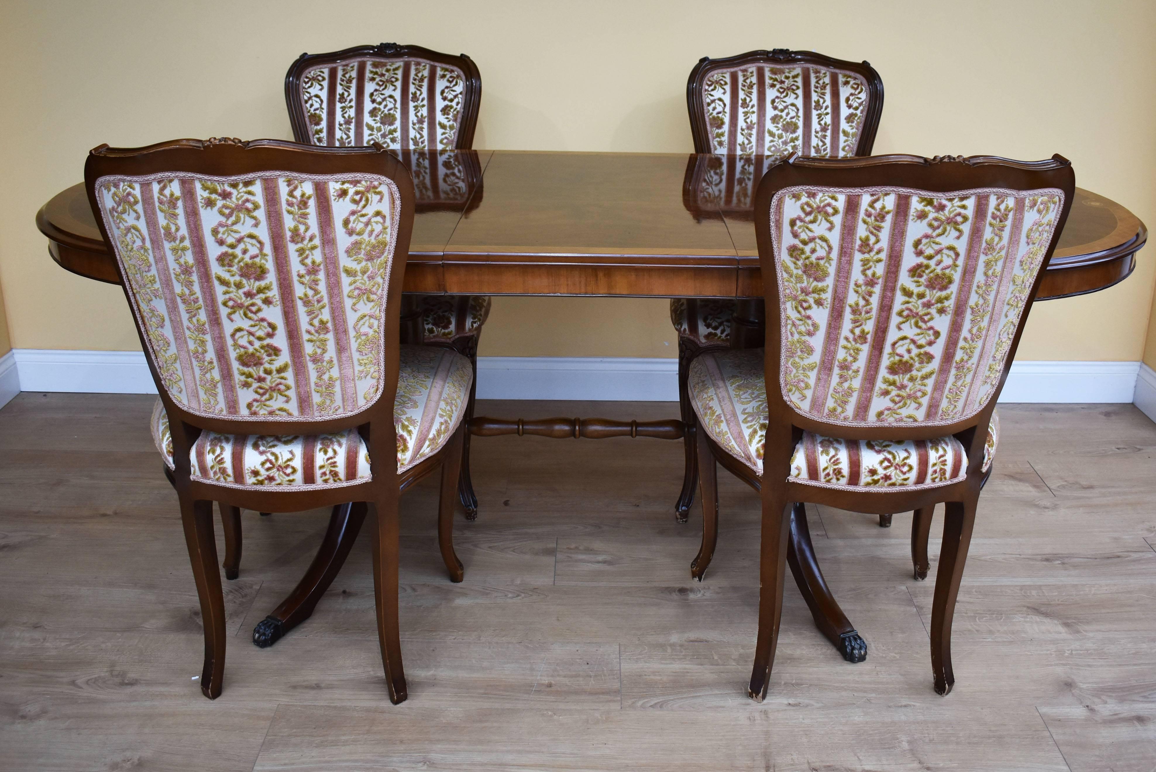 For sale is a fine quality Burr walnut dining table and six walnut dining chairs. The table has an additional leaf and stands on two pedestals, each with sweeping legs terminating on lions paw castors. The chairs have ornate carving to the top,