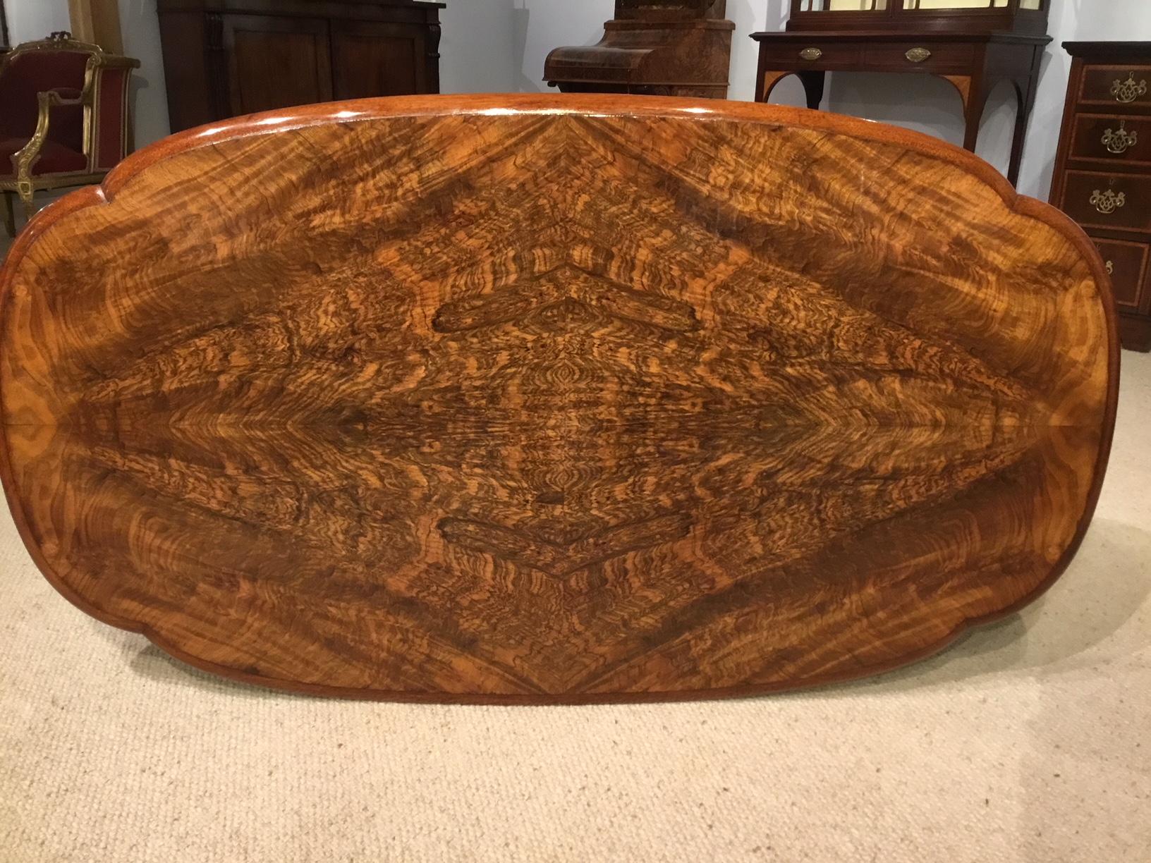 A beautiful burr walnut Victorian Period antique coffee table. Having an oval top veneered in beautifully figured burr walnut with walnut molding and frieze. Supported on four turned and fluted columns with finely carved floral detail and a central