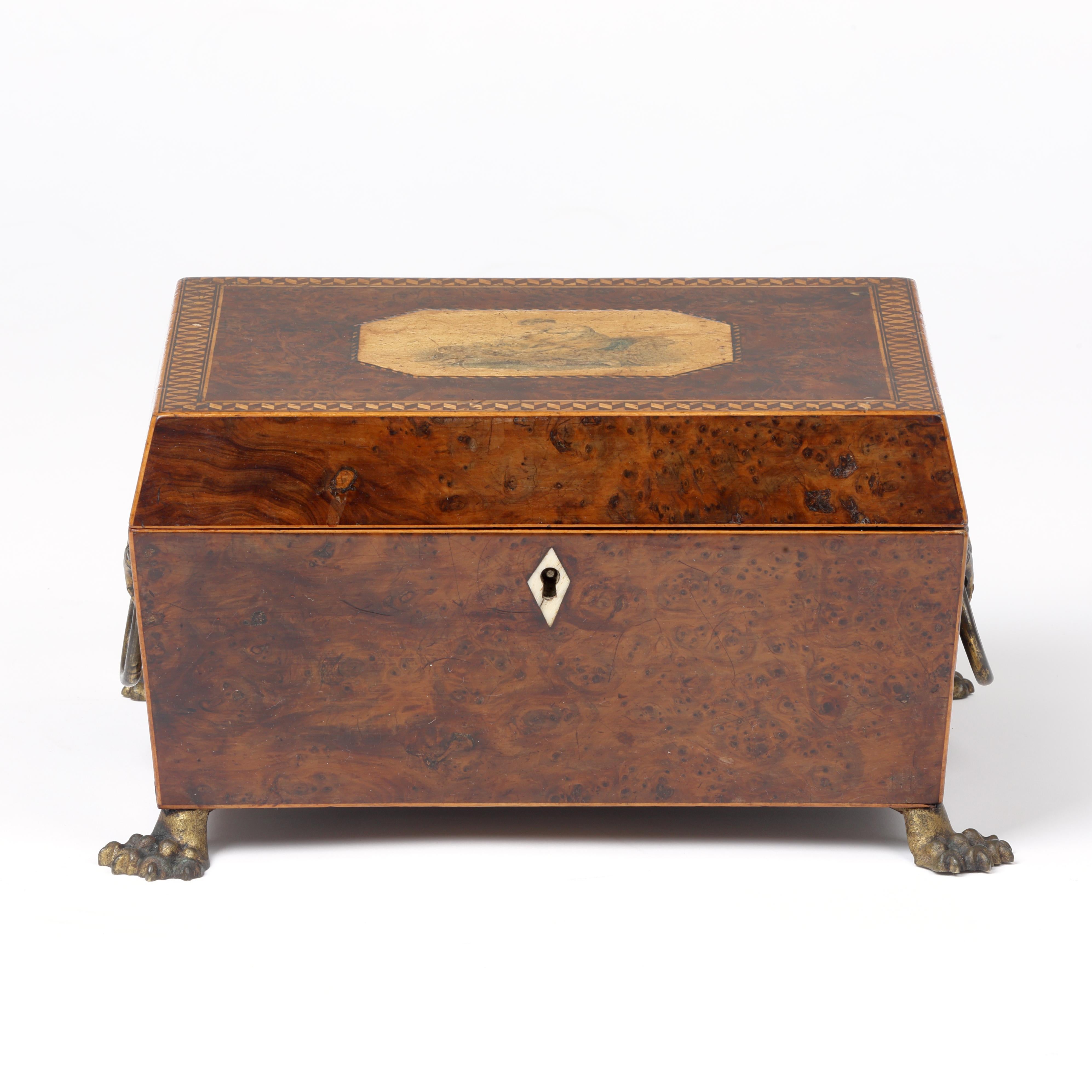 Boîte à bijoux ou à travaux d'aiguille en loupe d'if du début du XIXe siècle, dont le dessus est décoré d'une scène classique entourée d'un bandeau à damier.  Monté sur des pieds en pattes d'animaux en laiton.
