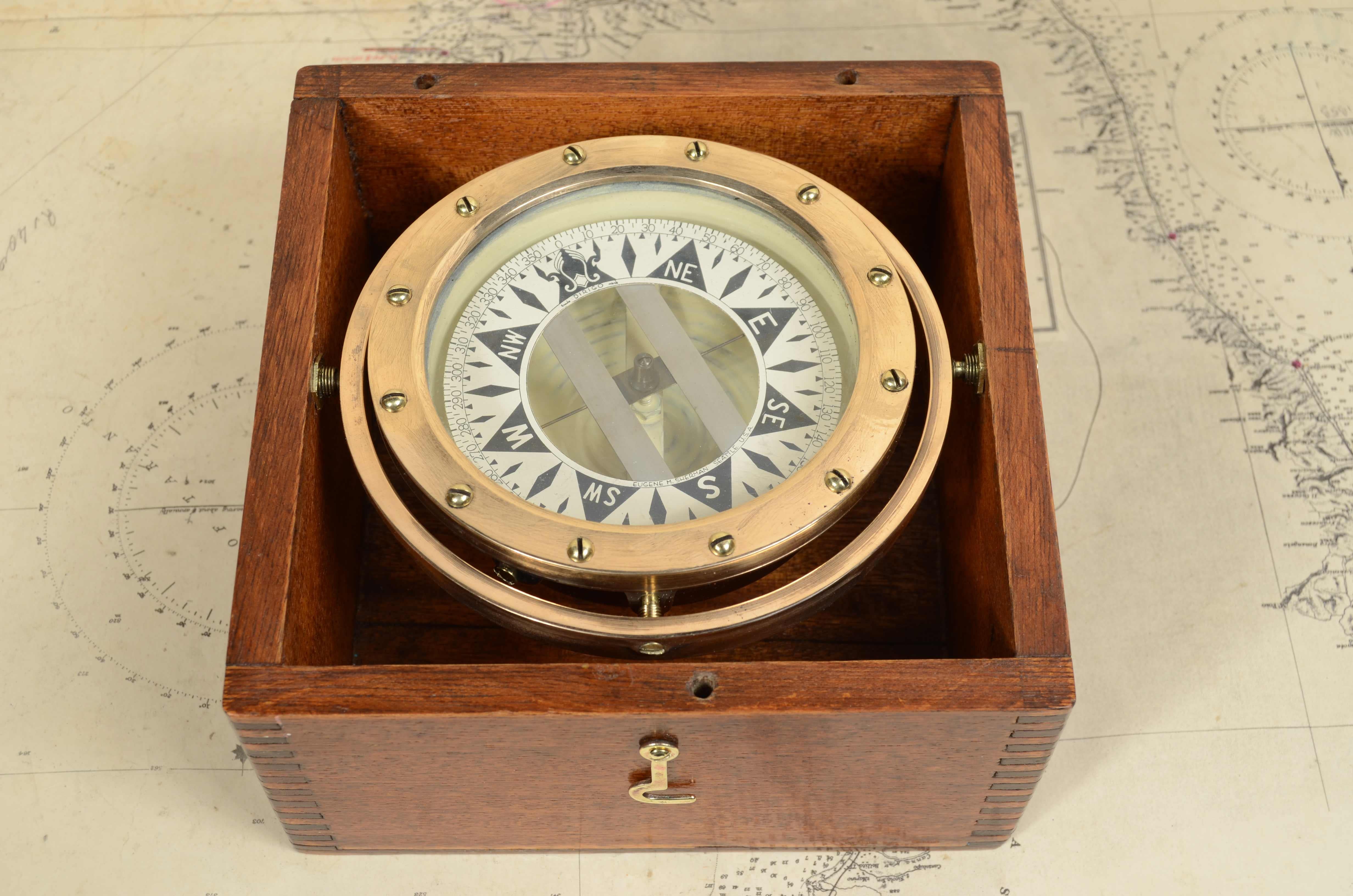 Nautischer Kompass aus Messing und Kupfer, kardanisch aufgehängt in der originalen Holzkiste mit Messingdeckelhaken, signiert Eugene M. Sherman Seattle  U.S.A.Trade Dirigo Mark aus den 1920er Jahren. Der Kompass besteht aus einem zylindrischen