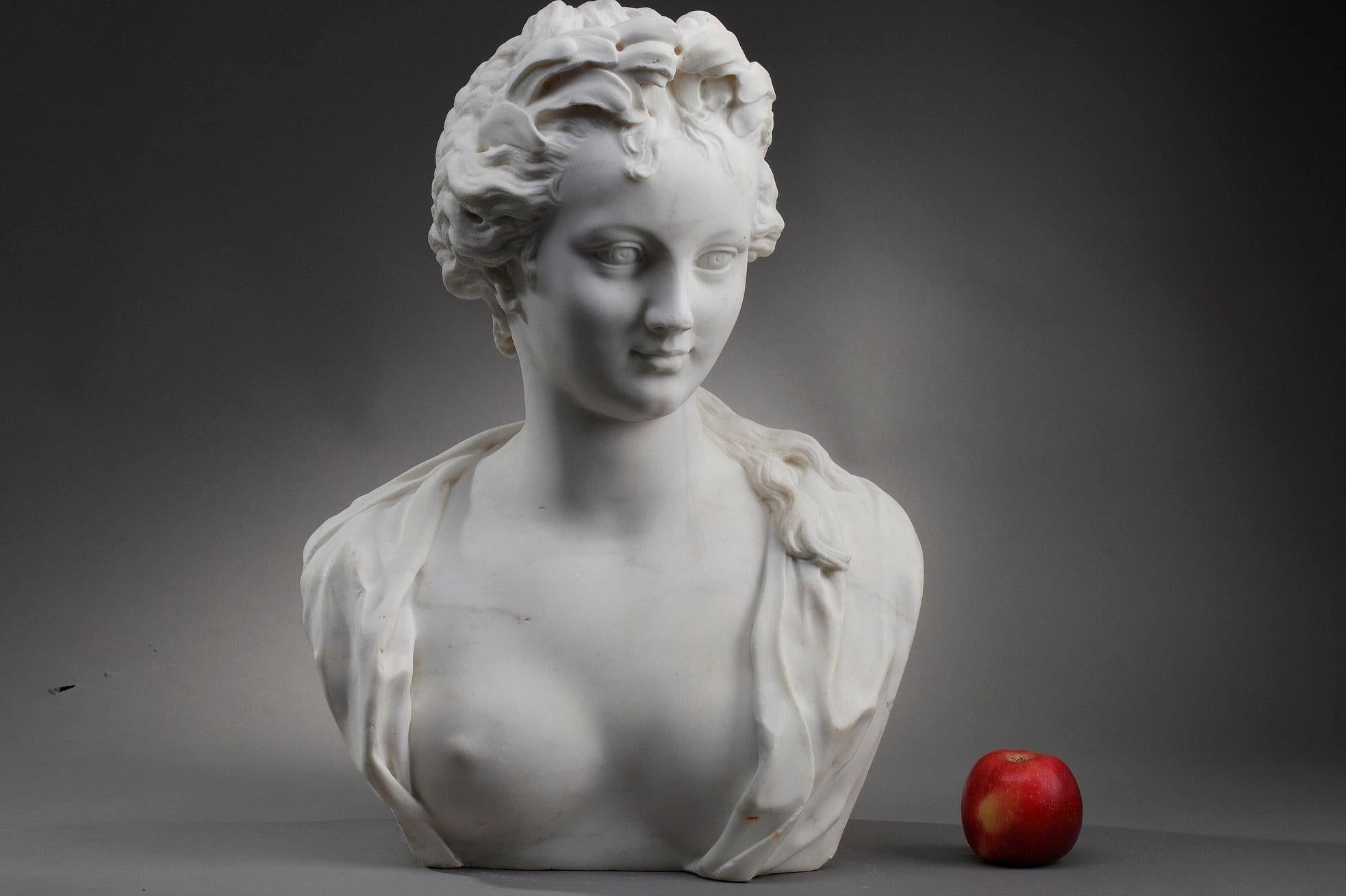 White marble bust representing a woman with a bare chest. The young woman looks to the right and smiles at us. Her hair is braided on her head and in a bun. The rest of her hair falls on her shoulder. This figure represents the allegory of Victory