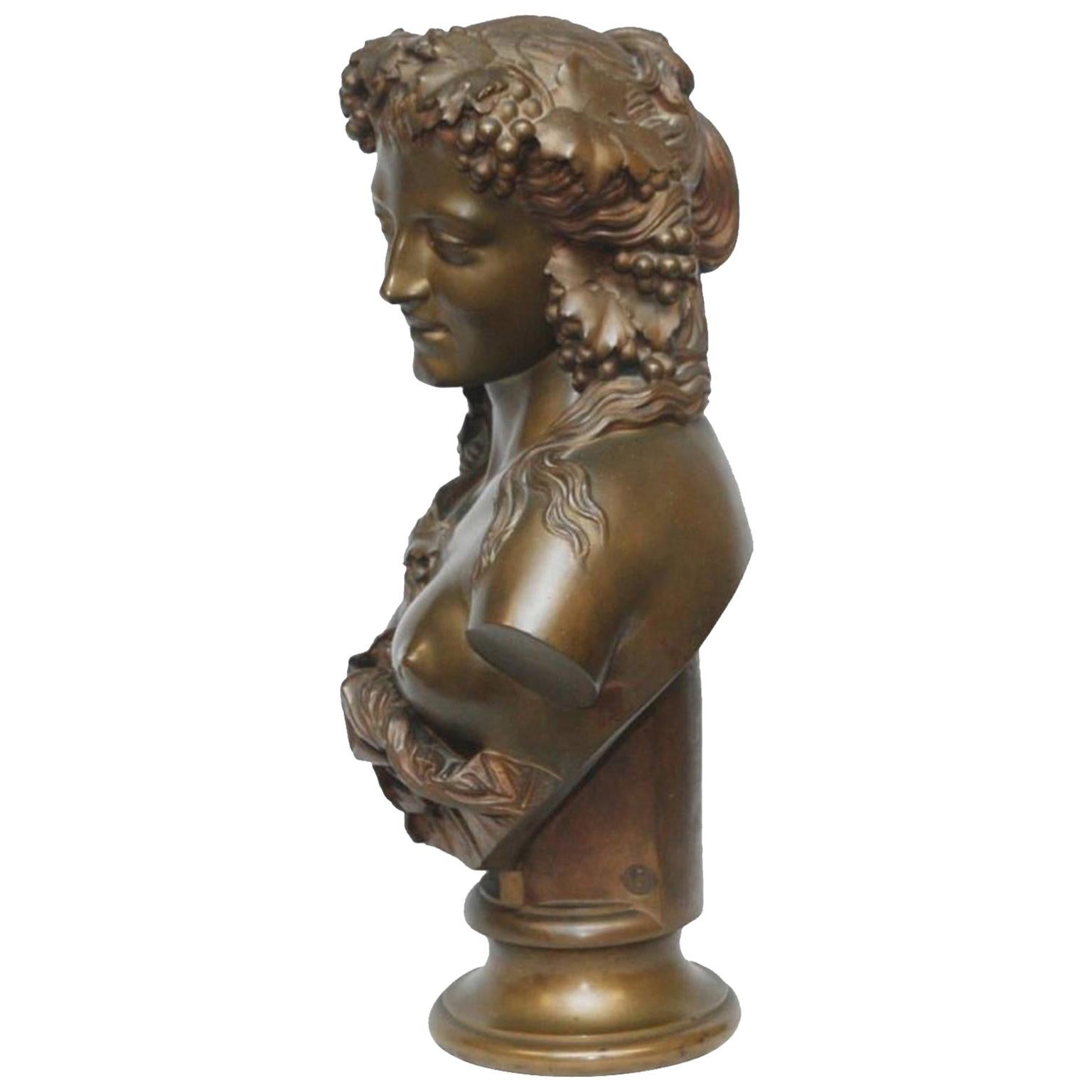 A large bronze bust showing a beautiful young woman depicted as a Bacchante, the Greek Goddess of Wine, her head festooned with grape branches. The bust is supported by an integral bronze plinth that at the back is inscribed with the name of the