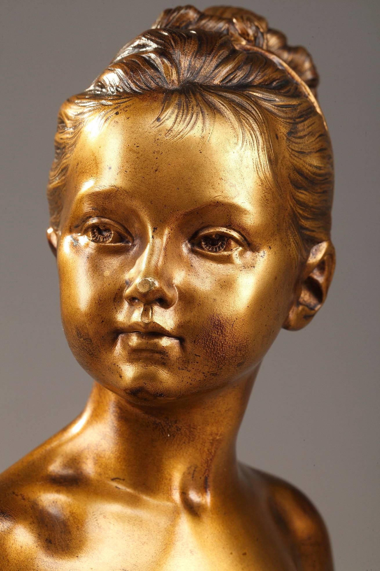 This small bust in bronze with gold patina derives from a masterpiece of children's portraiture by Jean-Antoine Houdon: the 