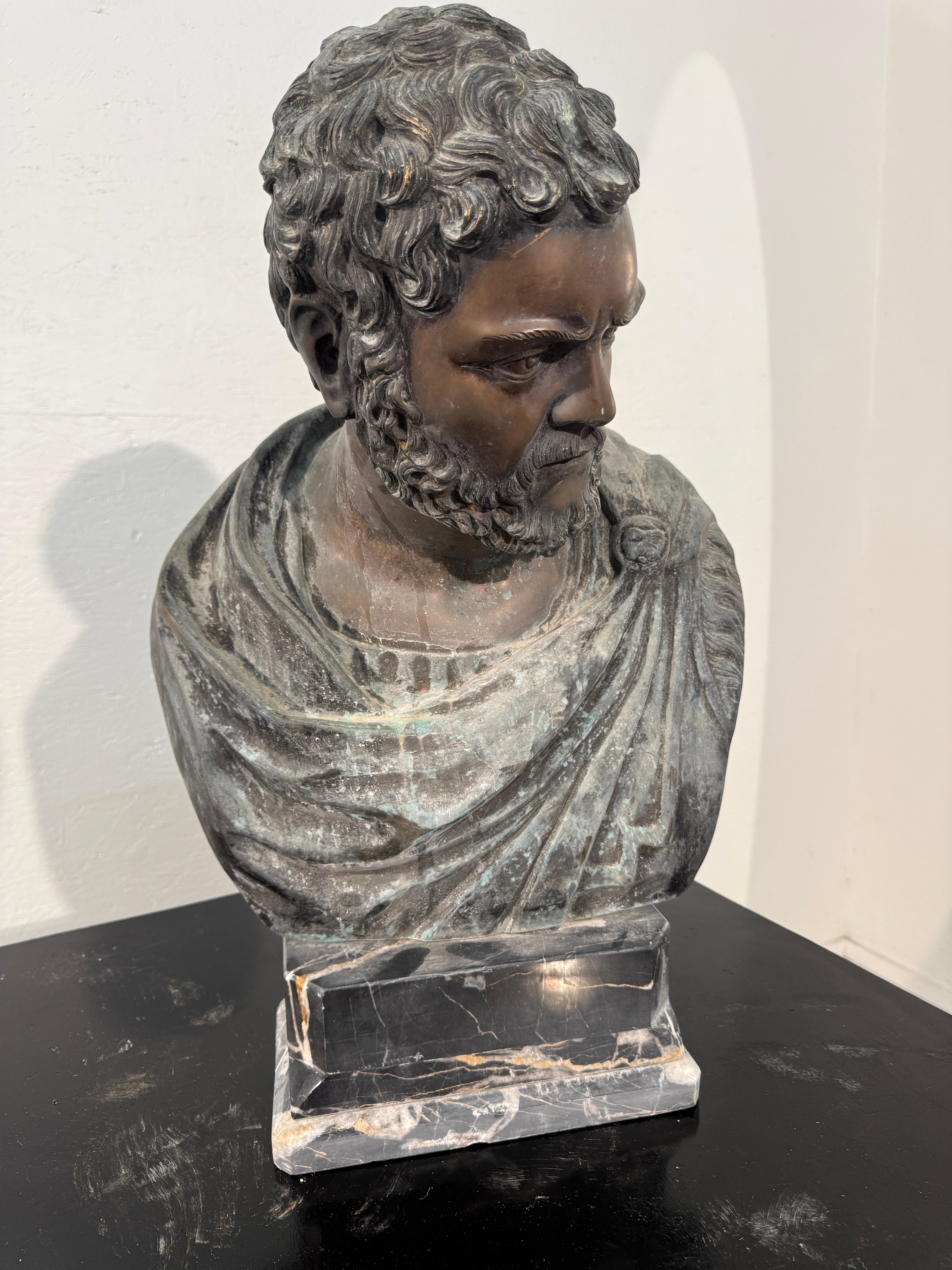 Buste imposant d'un philosophe ou d'un homme d'État romain, réalisé avec une finition patinée foncée qui accentue la profondeur des boucles et l'expression stoïque. La toge drapée est minutieusement détaillée, ses plis sont rehaussés par une subtile