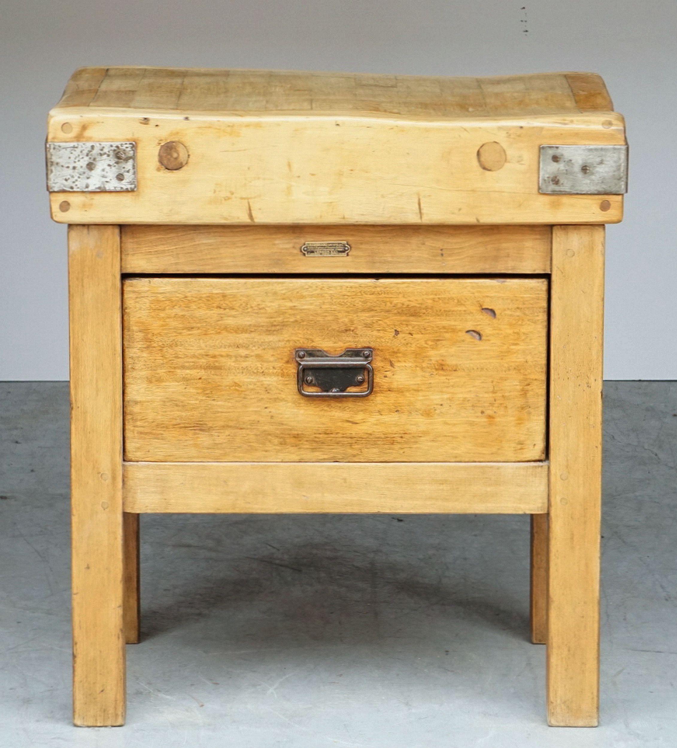 A two-tiered butcher's chopping block or table from England, featuring a large, rectangular sloping block or slab of iron-bound wood set upon a bottom tier four-legged, paneled support stand of pine, with fitted drawer and pull handles, the drawer
