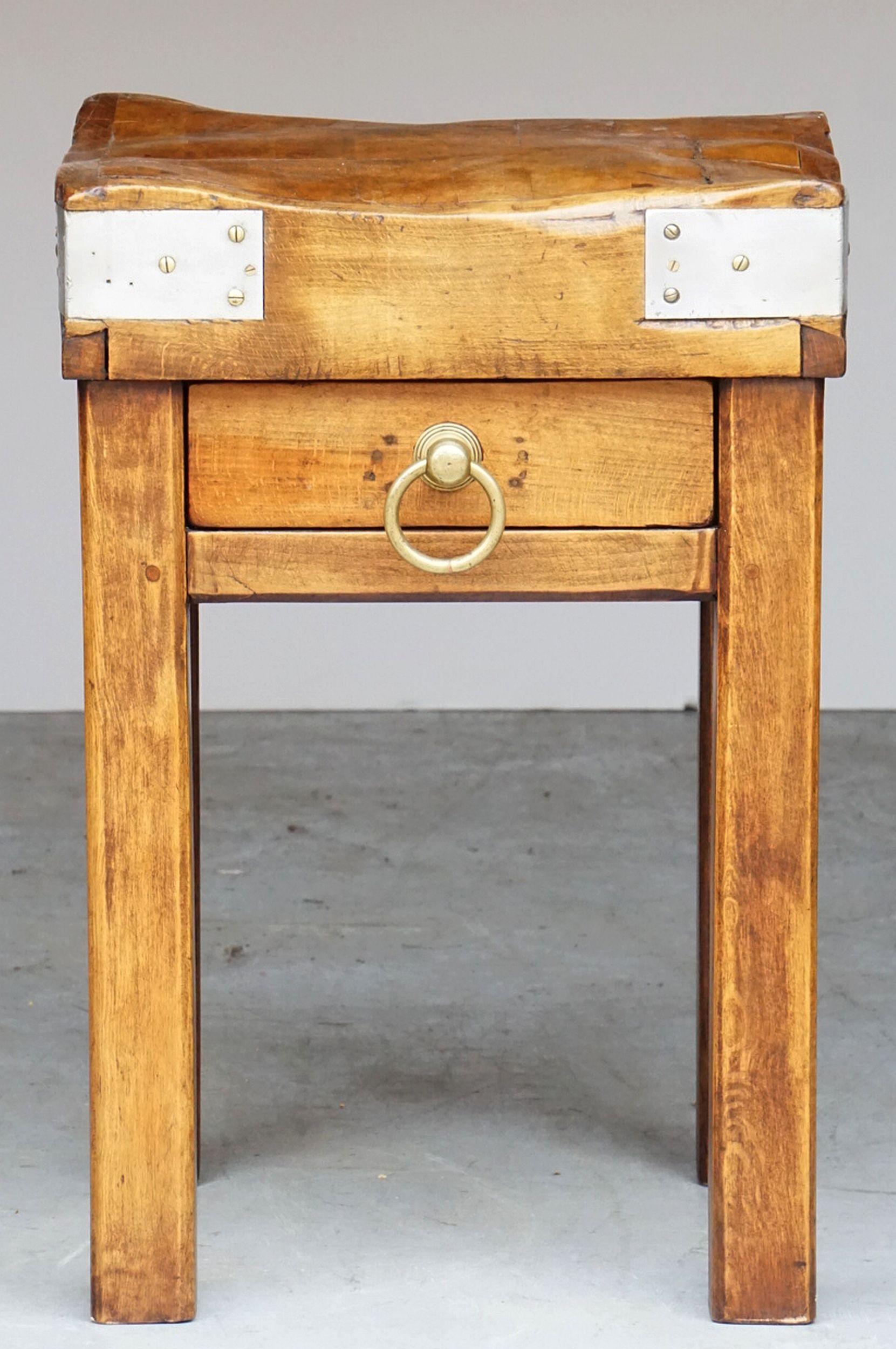 A fine French butcher's chopping block or table, featuring a large, square sloping block or slab of bound wood set upon a four-legged support stand of stained pine. Stand with drawer and large brass ring pull.

