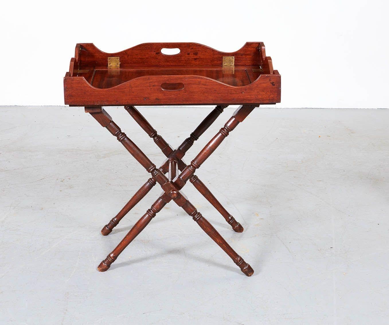 A high-quality mahogany bar stand, also known as a butler's tray, having four shaped and moveable sides secured by brass button locks and hinges, with carrying handles to two sides. The tray sits on a folding stand with canvas retaining straps. The