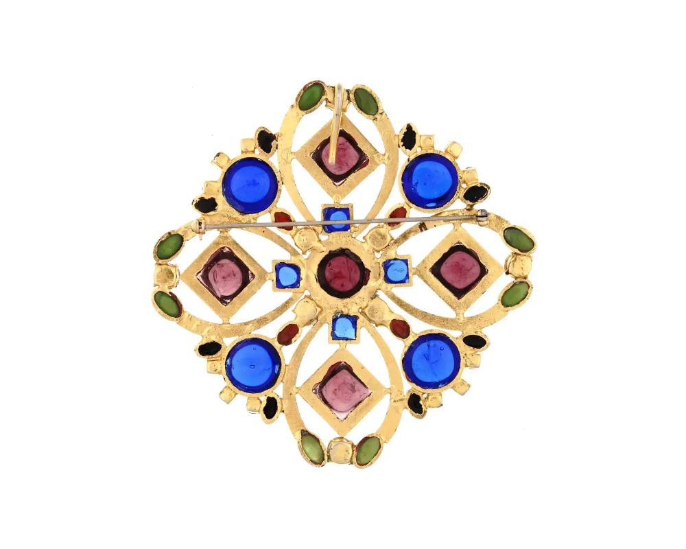 An impressive vintage Butler and Wilson English gripoix brooch pendant in gold tone metal set with bright blue, purple, and green poured glass cabochons and cut crystals. Features a pin and a chain bail to wear as a brooch or as a pendant. Note: