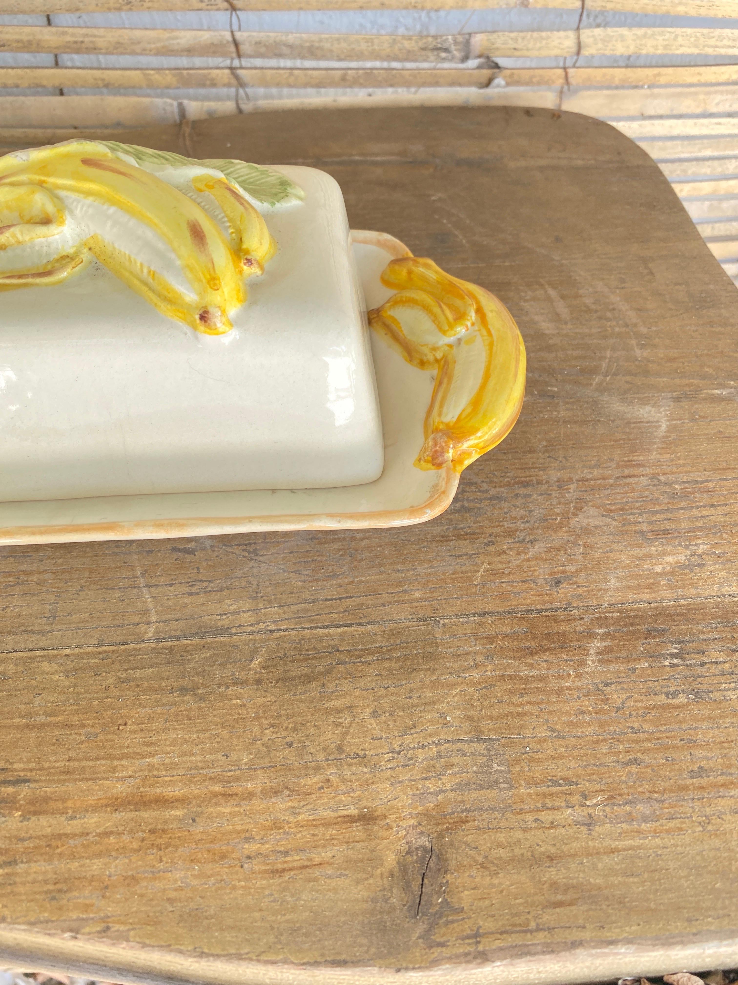 Diese Butterdose ist aus Keramik gefertigt. Es ist im Stil der Majolika gehalten. Hergestellt in Portugal in den 1970er Jahren. Er ist aus weißer und gelber Keramik gefertigt. Die Dekoration besteht aus gelben Bananen, die aus Keramik geformt sind.
