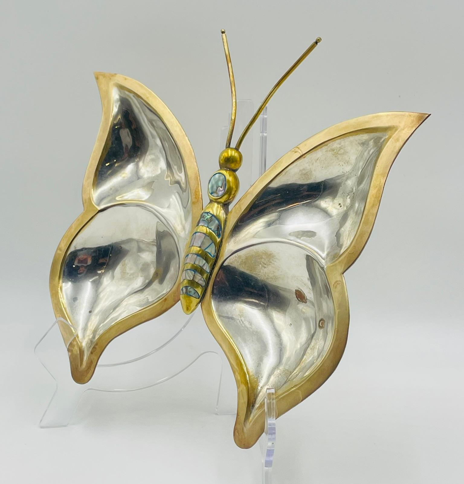 Stravagante piatto da portata o da immersione a forma di farfalla della metà del secolo scorso, realizzato a mano in Messico intorno agli anni Sessanta. Questo affascinante pezzo combina una lastra d'argento lucido con finiture in ottone e intarsi