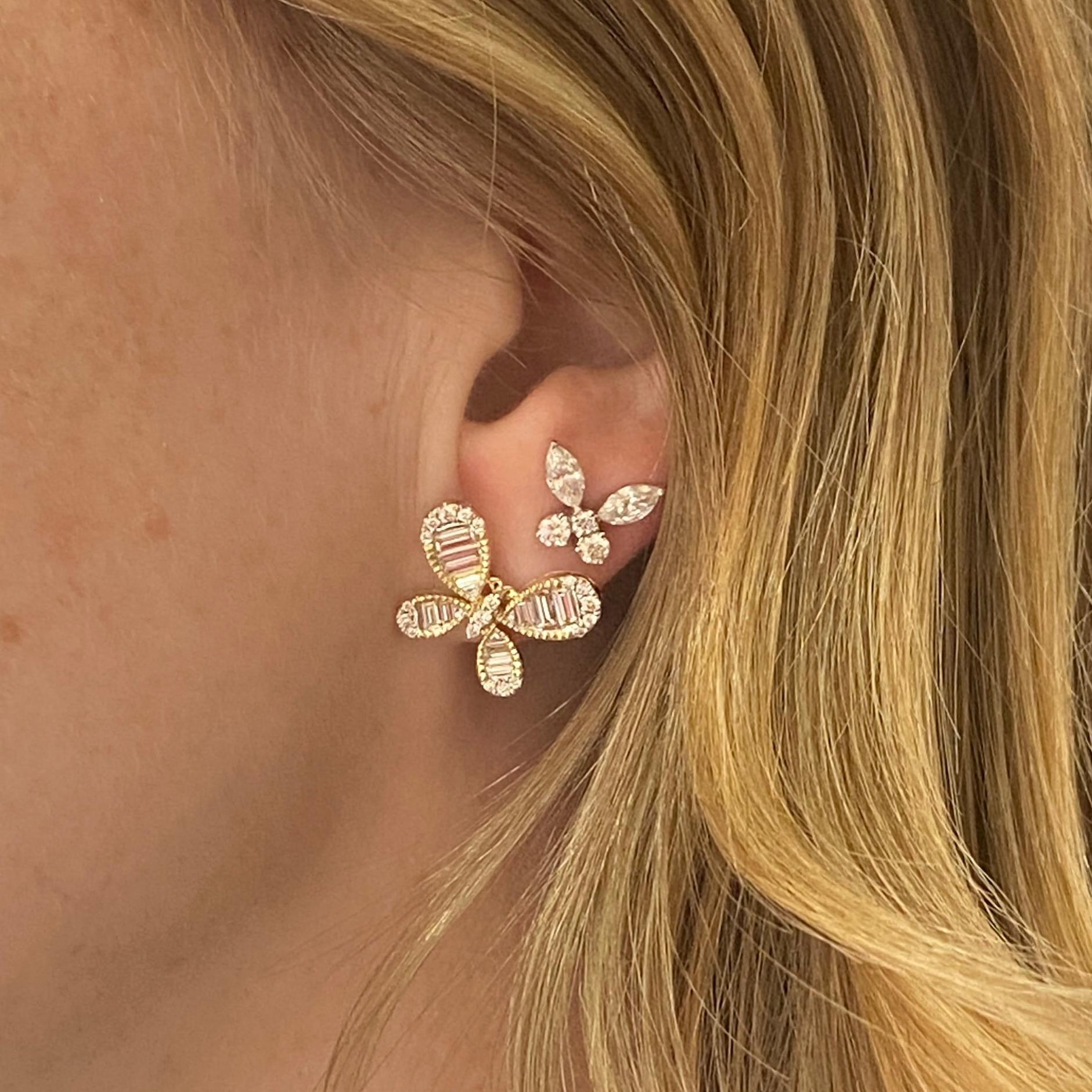 Ces magnifiques et audacieux clous d'oreilles en forme de papillon sont artistiquement conçus avec une pile diagonale de diamants baguettes qui donnent vie au papillon. Les accents de diamants ronds gradués et les détails perlés sur la monture en or