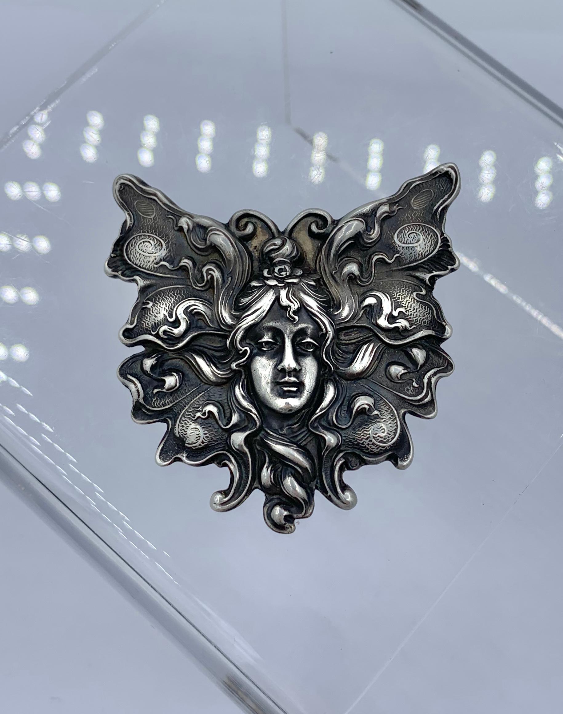 This is a museum quality Art Nouveau Brooch in Sterling Silver depicting a butterfly fairy maiden woman by Unger Brothers. 
This rare and extraordinary motif is rendered with exquisite Art Nouveau beauty.  The fairy maiden's hair flows into the