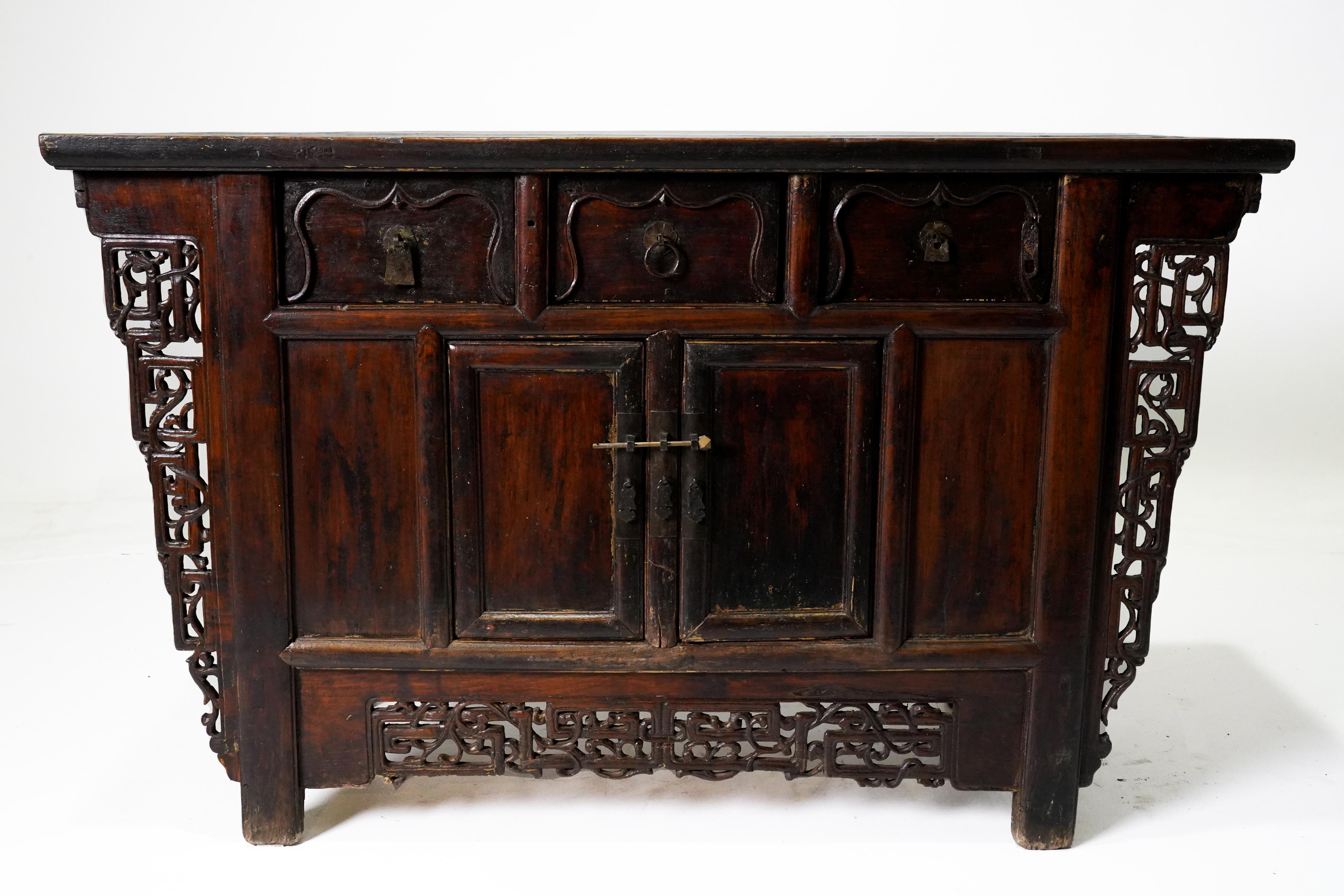 A Chinese Ming-style wooden butterfly cabinet from the 19th century, with carved spandrels, drawers, doors and dark oxblood patina. This elegant coffer, called a butterfly cabinet, features a rectangular floating panel top sitting above three