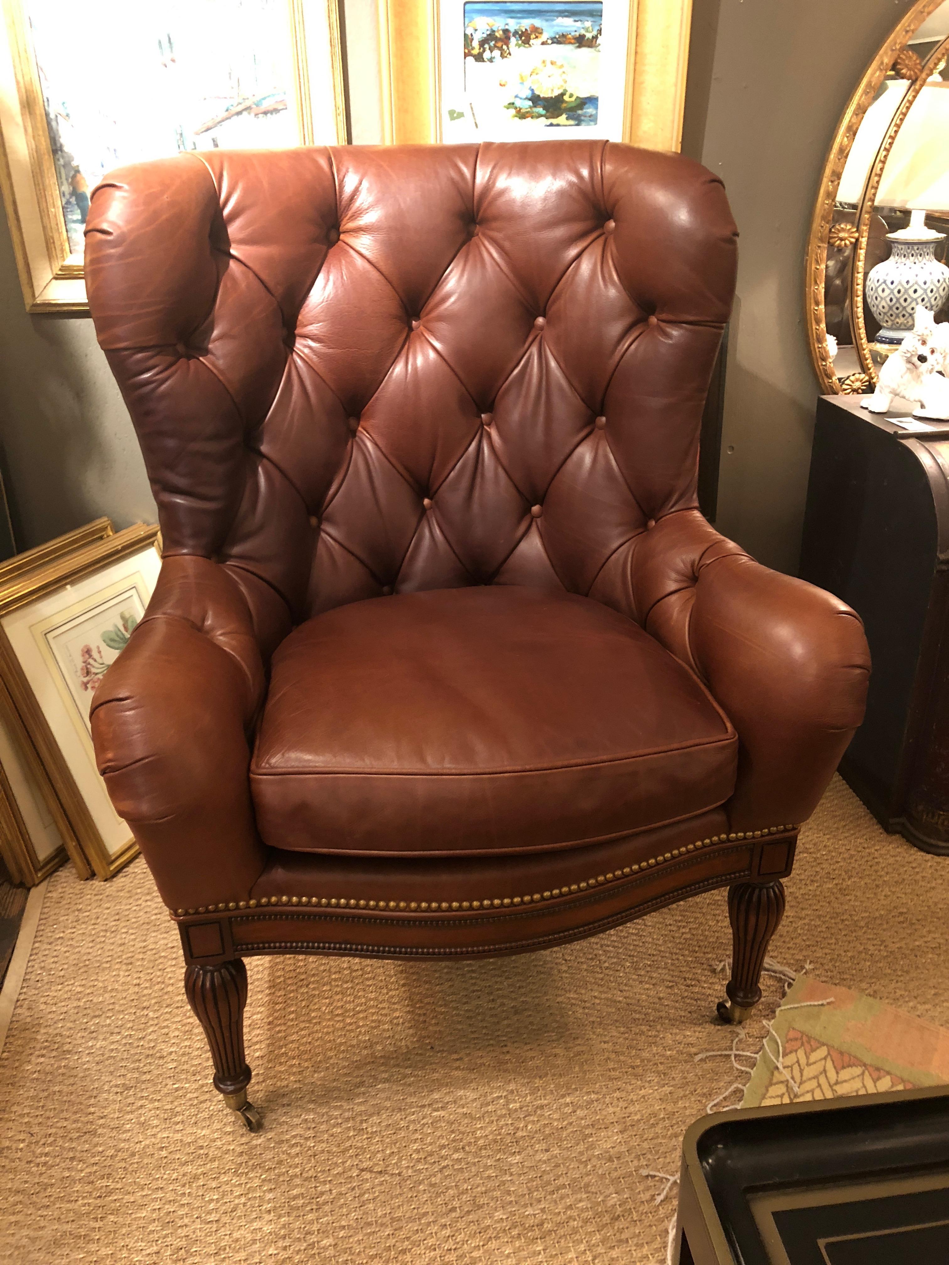 A very handsome Beacon Hill supple brown leather wing chair having button tufting on the inside back, brass nailhead detailing, detachable seat cushion with partial down interior, shapely mahogany legs and brass casters on the front two feet. Super
