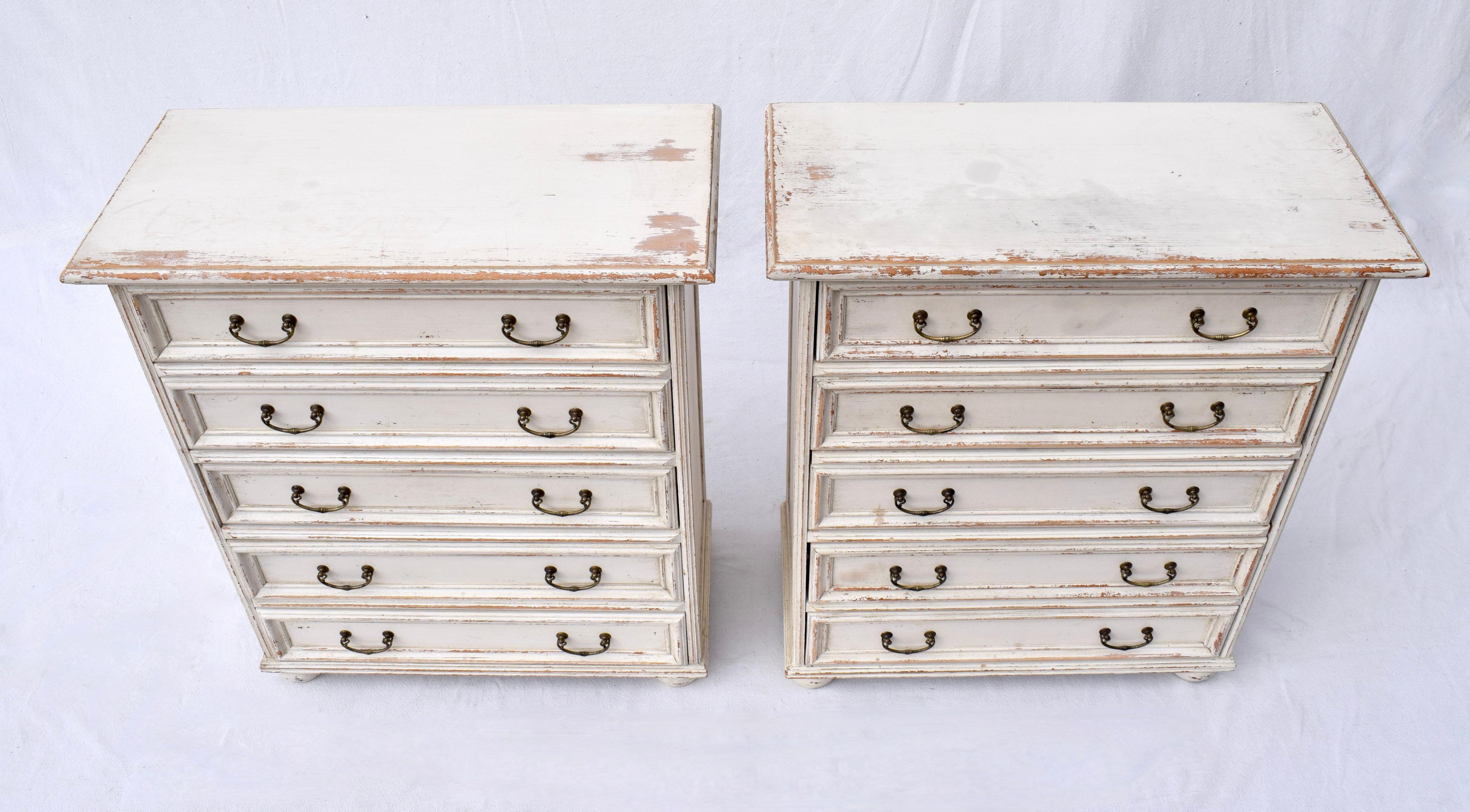 A pair of chests of five paneled drawers with bun feet & brass pulls made in Italy by Buying & Design boasting intensionally distressed whitewash finish; circa late 1990's. Beautifully maintained, ready for use.