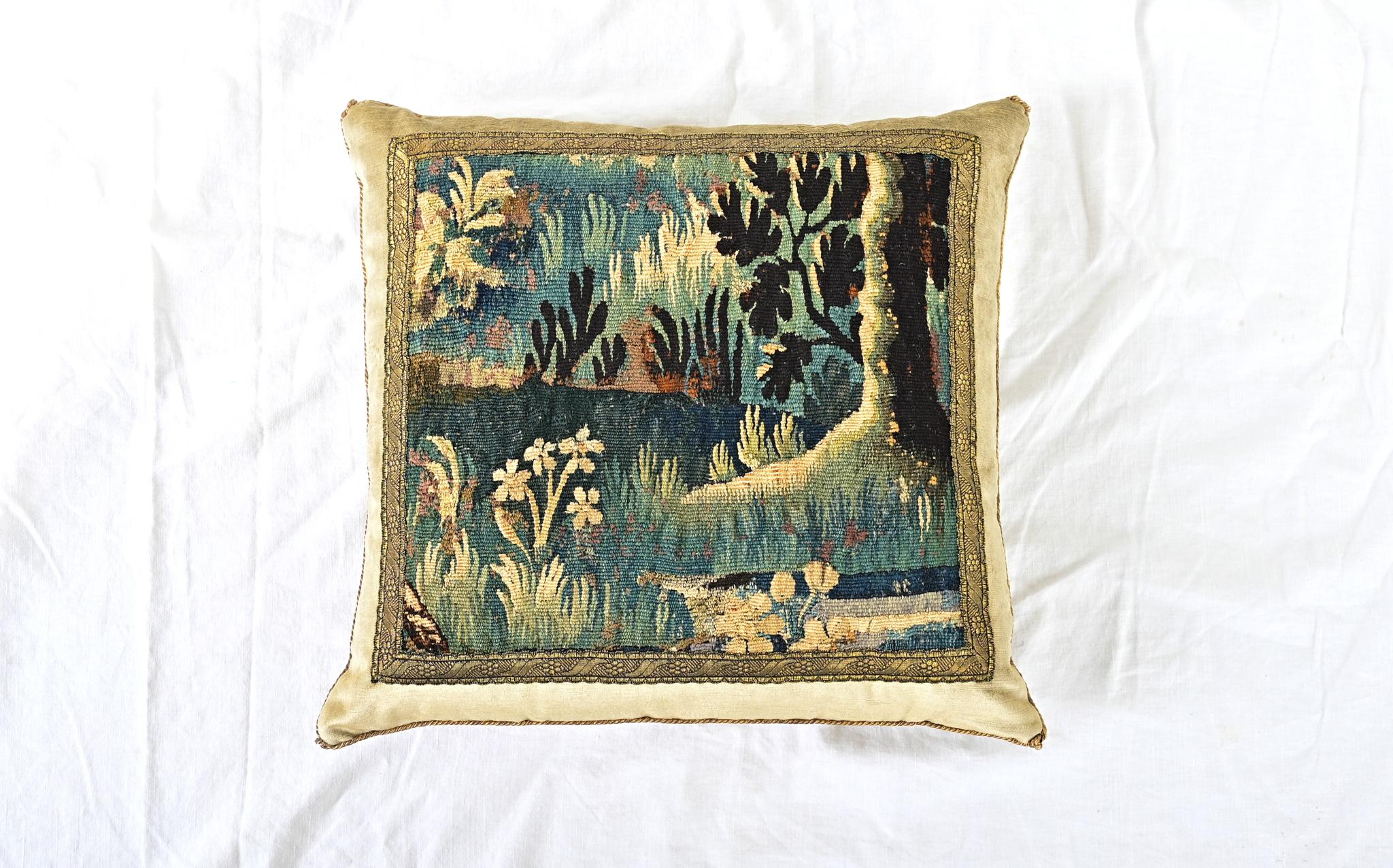 Coussin récemment confectionné à partir d'un fragment de tapisserie ancienne de la tradition d'Aubusson-Verdure (France, XVIIIe siècle) représentant une scène de forêt dans des tons or, vert, bleu et brun, encadré d'une garniture en galon (ou
