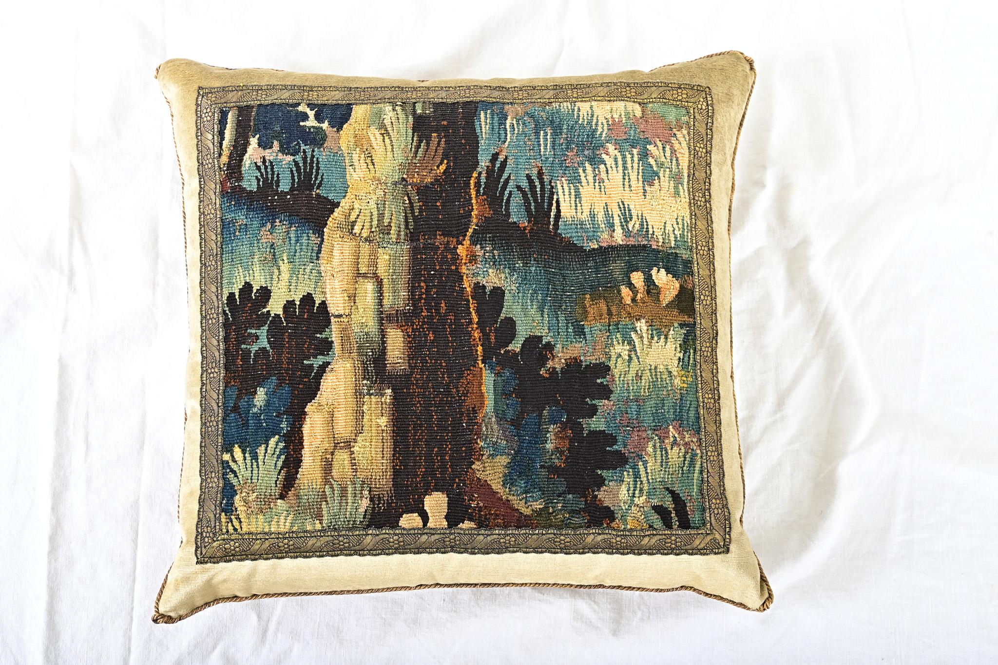 Coussin récemment confectionné à partir d'un fragment de tapisserie ancienne de la tradition d'Aubusson-Verdure (France, XVIIIe siècle) représentant une scène de forêt dans des tons or, vert, bleu et brun, encadré d'une garniture en galon (ou
