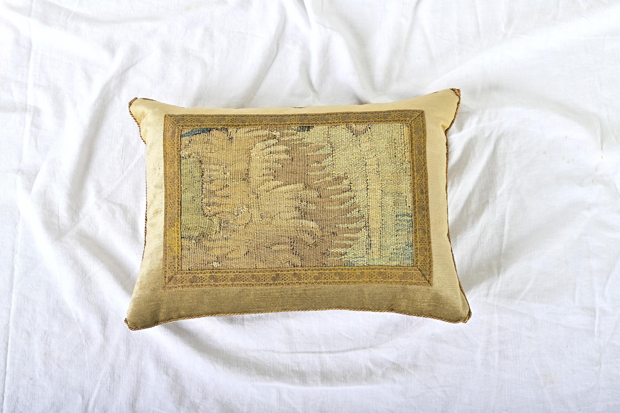 Coussin récemment confectionné à partir d'un fragment de tapisserie ancienne de la tradition d'Aubusson (flamande, XVIIe siècle) dans des tons d'or, de vert, de bleu et de brun, encadré d'un galon (ou d'une galonnade) métallique d'or ancien sur un