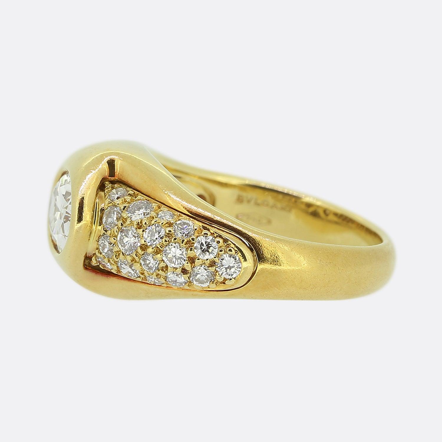 Here we have a highly impressive and rare diamond ring from the world renowned Italian jewellery house of Bvlgari. A single oval faceted 1.01ct diamond sits proud in a rub-over setting at the centre of the face which is complimented by pavé diamond