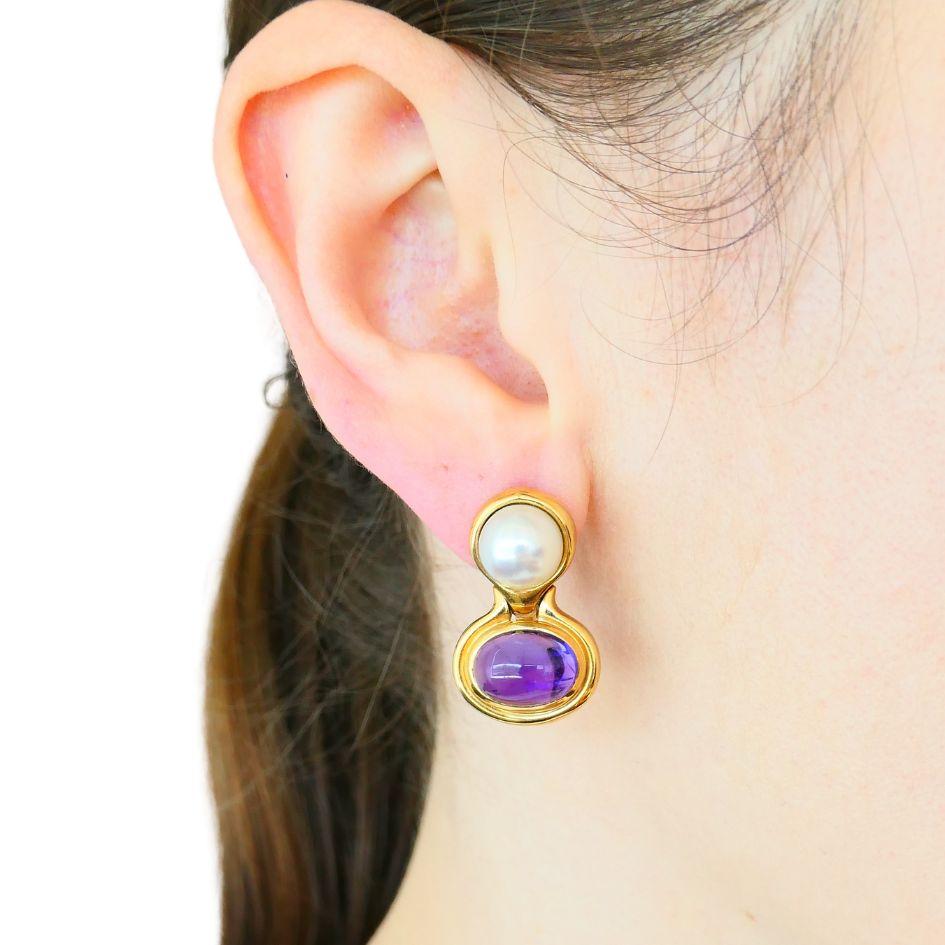 This pair of vintage Bvlgari earrings is crafted in 18k yellow gold and dates to circa the late 1980s to early 1990s. The design features luminous cultured pearls set above rich oval cabochon amethysts, all within rounded bezels that exemplify