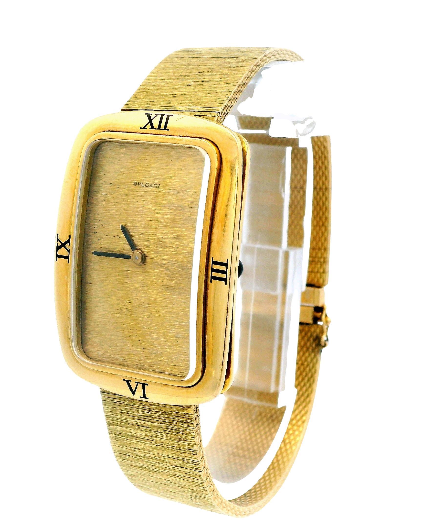 The Bvlgari watch features a long cushion-shaped case measuring 27 mm by 38 mm from lug to lug. It is crafted from 18K yellow gold and has a bezel adorned with four Roman numeral enamel hour markers. The champagne-colored mesh dial is signed by