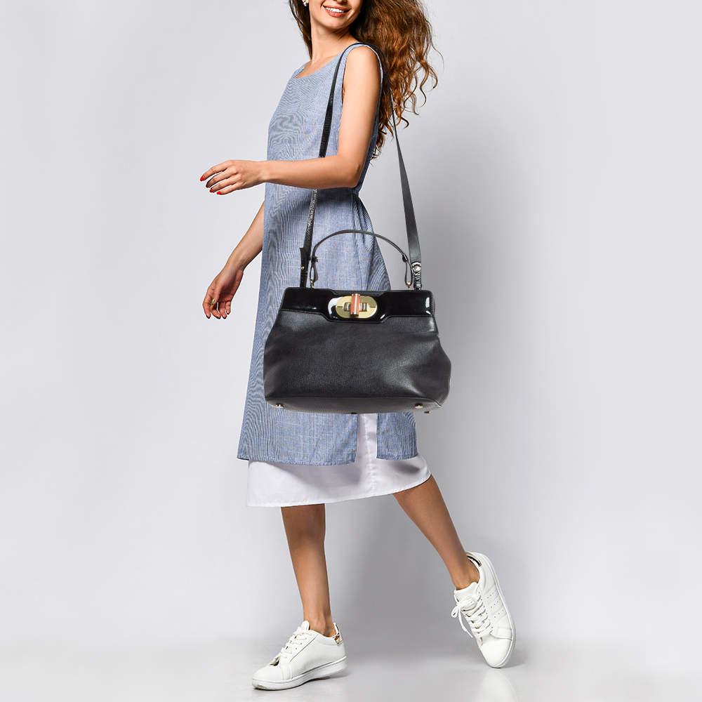 This Rossellini tote from Bvlgari is crafted from black leather and has a well structured design. The bag comes with protective metal feet and a top handle along with a shoulder strap. The turn lock closure opens to a fabric lined interior capacious
