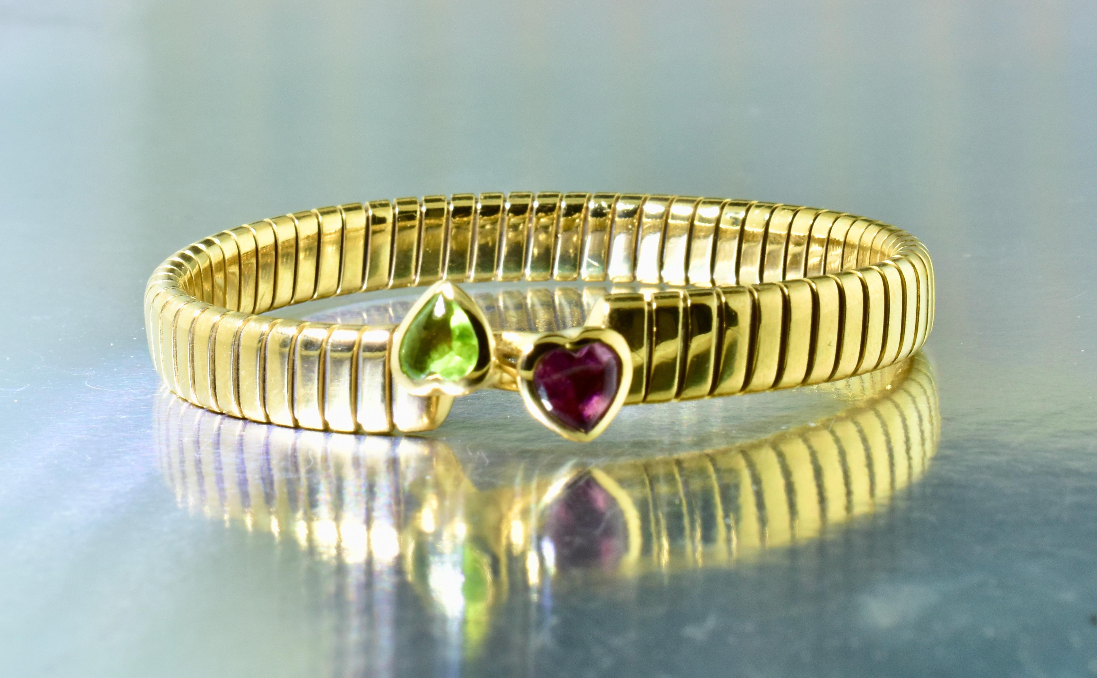 Bulgari tubogas bracelet in 18K yellow gold with natural heart shaped green peridot and pink natural tourmaline.   These stones are well cut and approximately 1 ct. each. This cuff bracelet which has a closure by interlocking the two heart shapes -