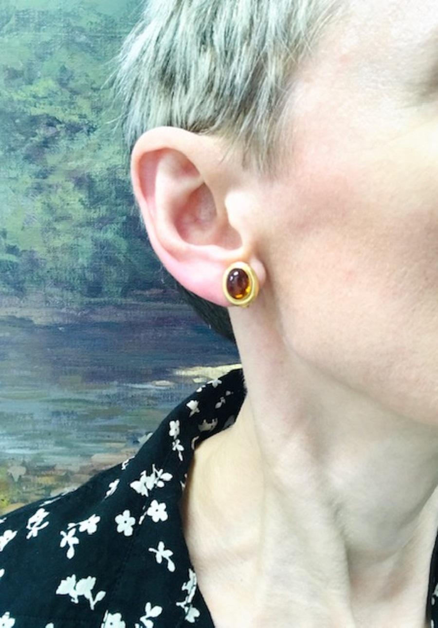 Ogni orecchino presenta un citrino cabochon di forma ovale incastonato in un castone d'oro liscio. Il citrino ha una tonalità ambrata e una finitura lucida. Le cornici in oro sono leggermente bombate e rispecchiano la forma delle pietre. Disegnati