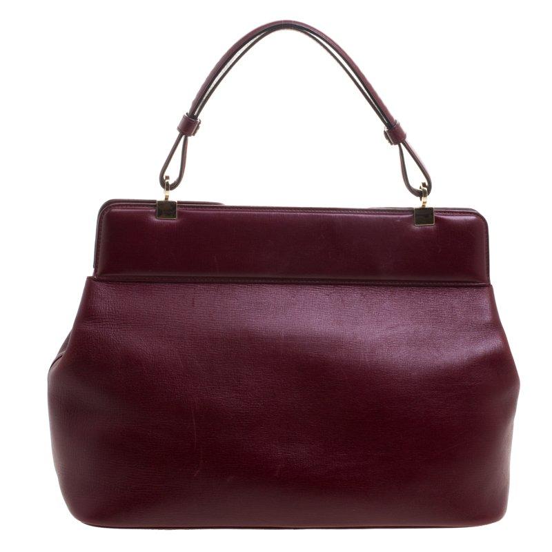 This Rossellini tote from Bvlgari is crafted from burgundy leather and has a well structured design. The bag comes with protective metal feet and a top handle. The turn lock closure opens to a fabric lined interior capacious enough to carry your