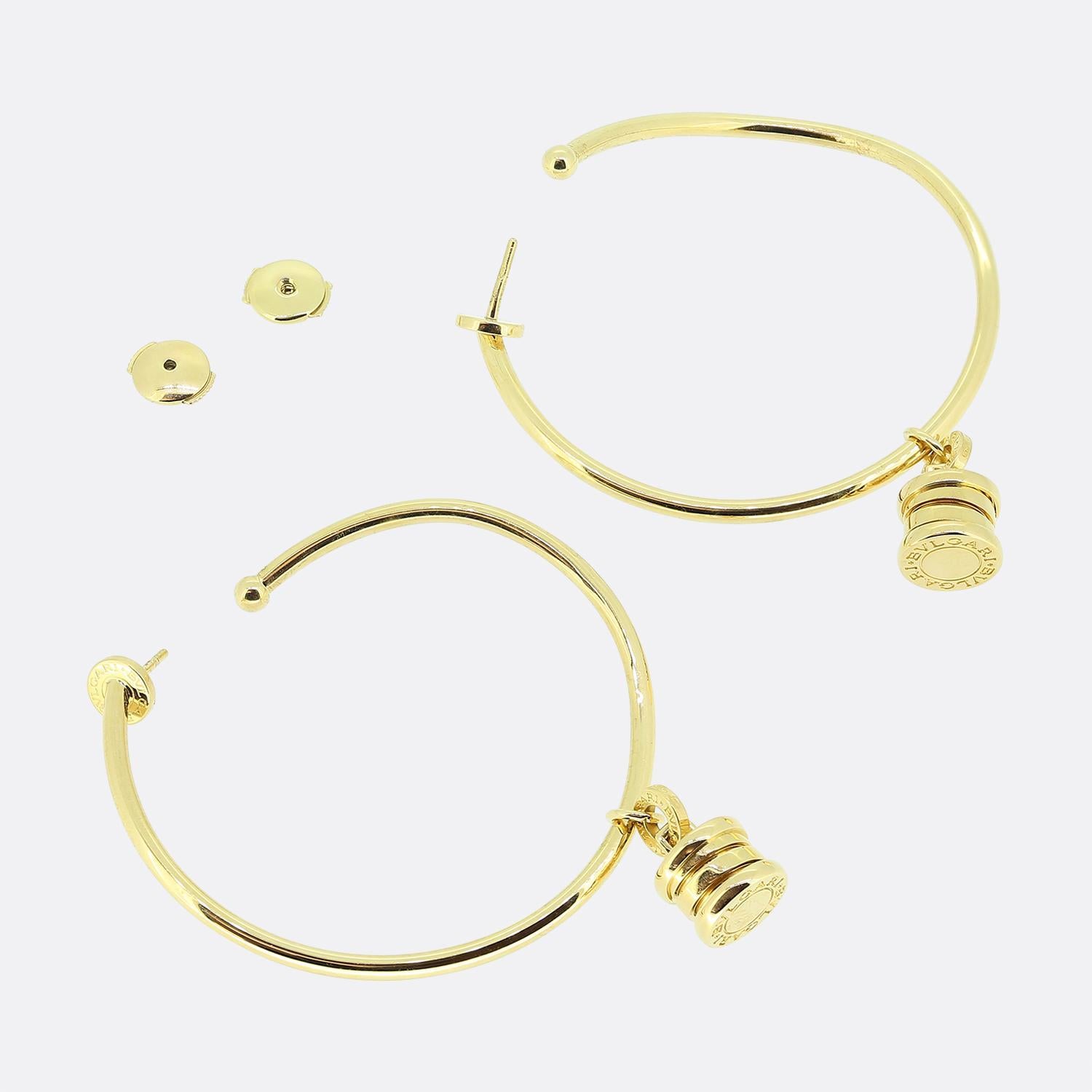 This is a striking pair of hoop earrings from the world renowned jewellery house of Bvlgari. Each identical piece has been made from a rich 18ct yellow gold and features a sleek, polished hoop design. Dangling from each hoop is a cylindrical charm