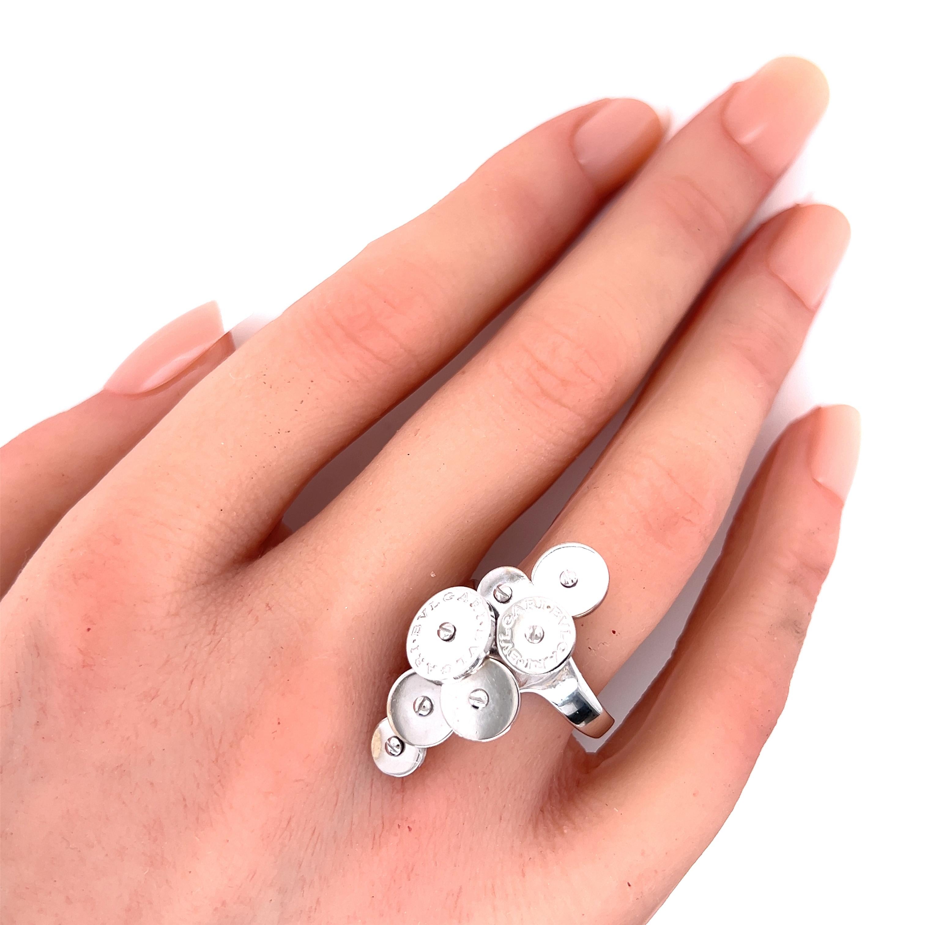 Questo è un anello autentico di Bvlgari della Collection'S. È realizzato in oro bianco 18 carati con finitura lucida e presenta dischi multipli sovrapposti su due file, due dischi più grandi con inciso Bvlgari. L'anello è firmato dal designer con il