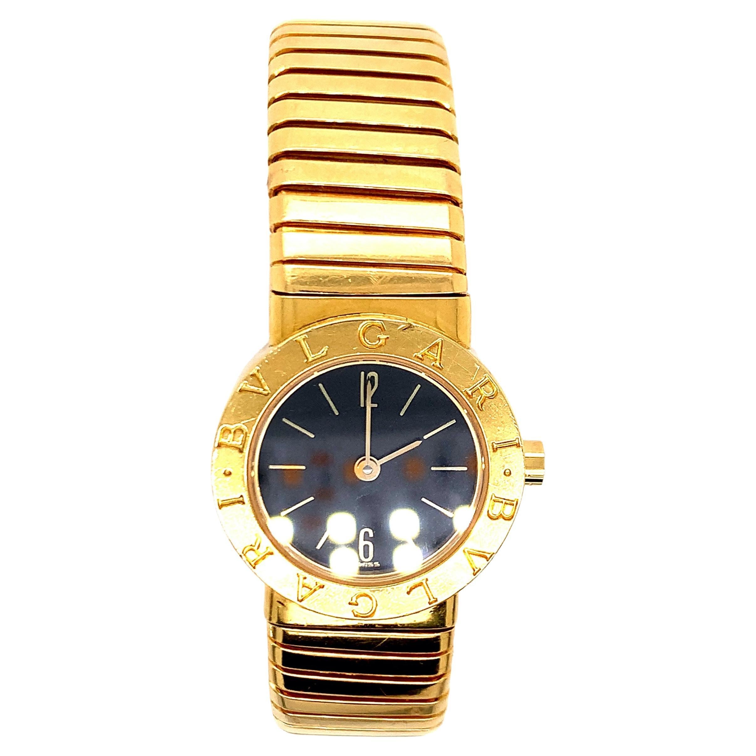 An 18 karat gold ‘Tubogas’ bangle watch created by Bvlgari and made in Switzerland. The open-ended bracelet has a round black dial at its center, with baton chapters and Arabic numerals at twelve and six. The movement is quartz. 

Serial no. BB 23