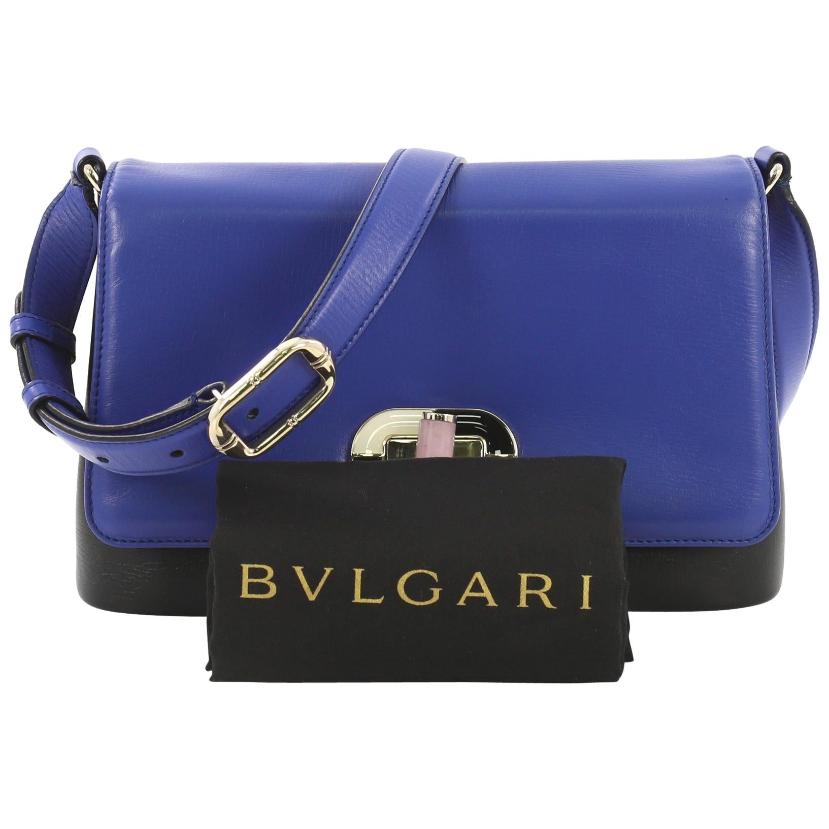 This Bvlgari Icona Shoulder Bag Leather Medium, crafted from blue and black leather, features a leather shoulder strap, exterior back slip pocket, and gold-tone hardware. Its turn-lock closure opens to a blue fabric interior with two compartments