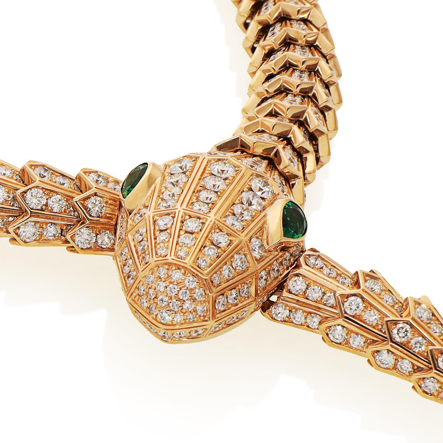 Crafted as a mesmerizing overlapping serpent, the piece features shimmering scales adorned with circular-cut diamonds that catch and reflect light from every angle. Its striking pear-shaped emerald eyes lend an enchanting touch of color, drawing the