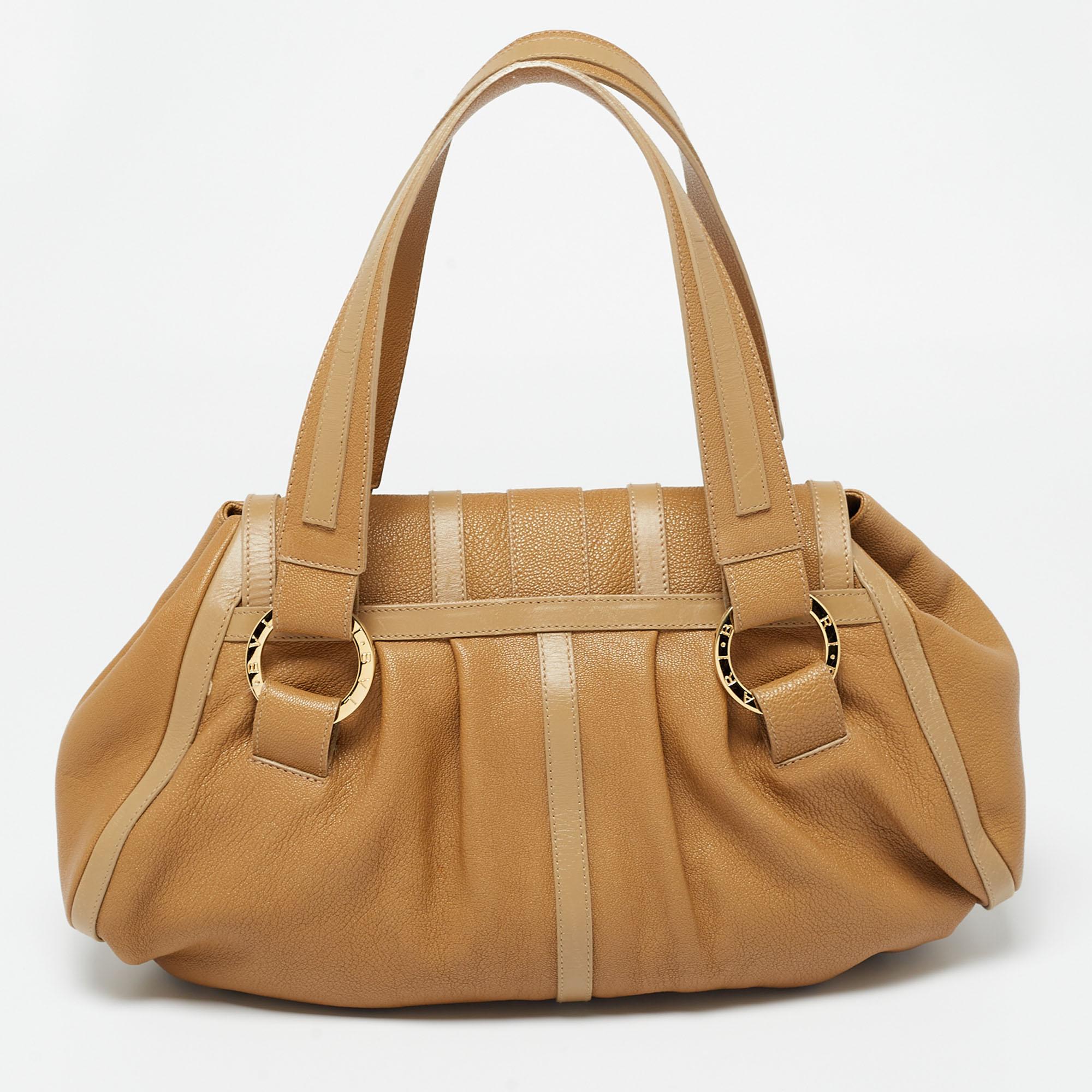 This shoulder bag from Bvlgari is a fabulous piece. It has been crafted from leather in a gorgeous tan shade and is equipped with two handles and gold-tone accents. The spacious interior comes with a zipped pocket.

Includes: Info Booklet