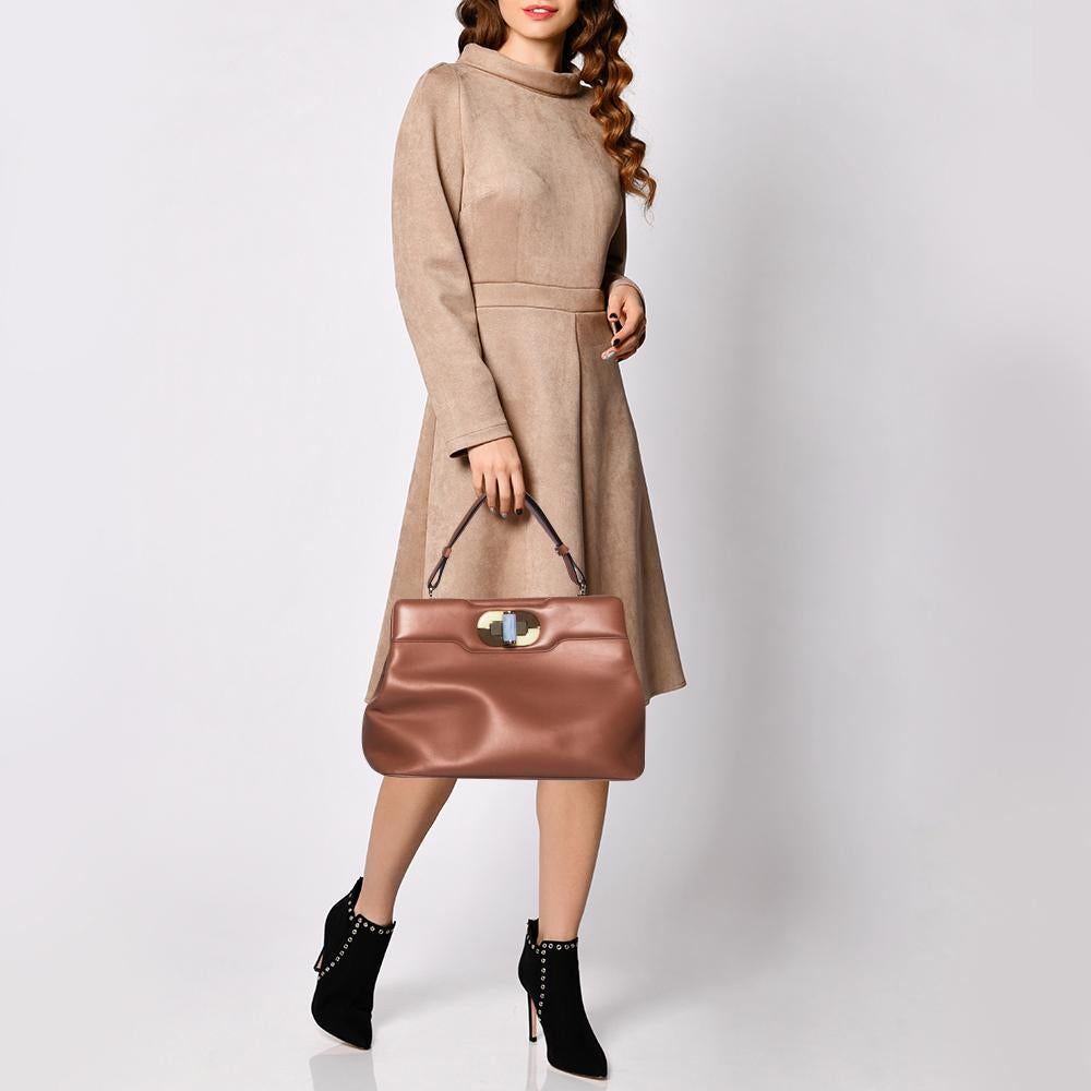 This Isabella Rossellini bag from Bvlgari is crafted from tan leather and has a refined design. The bag comes with protective metal feet and a top handle. The turn-lock closure opens to a fabric-lined interior capacious enough to carry your