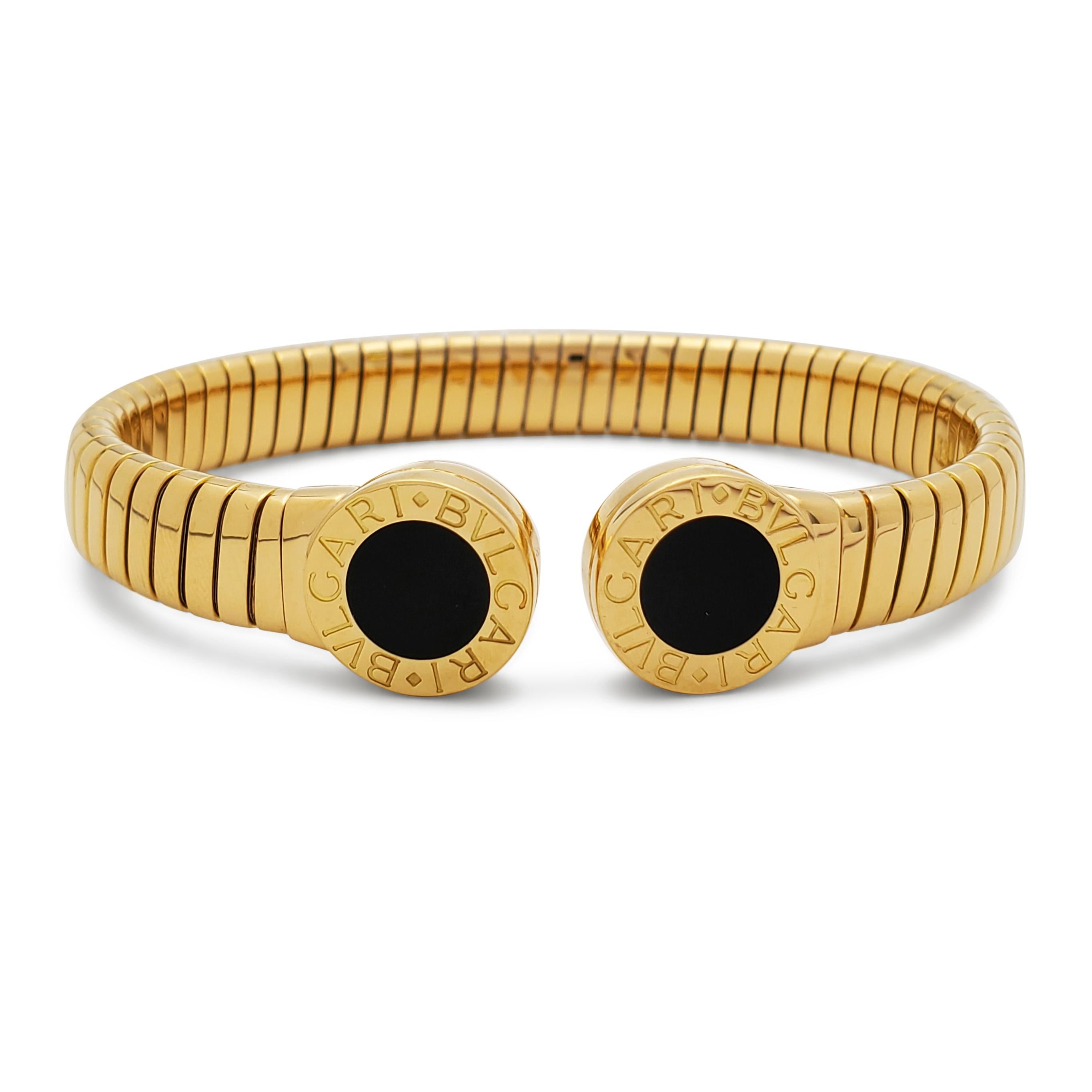 Authentic Bvlgari 'Tubogas' bangle bracelet crafted in 18 karat yellow gold with stainless steel interior mechanism.  A circular onyx stone is set at each end of the split bracelet.  The bracelet measures 8.4mm in width and will fit up to a size 6