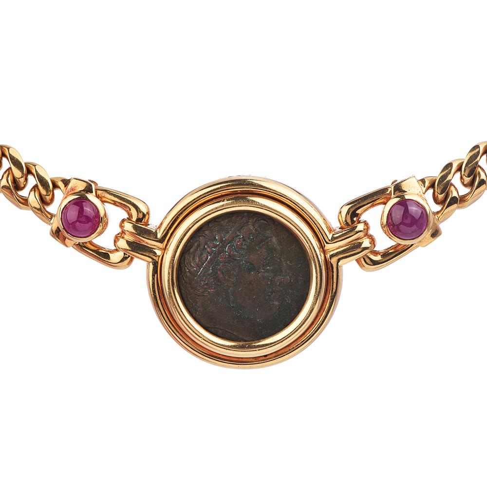  This vintage Bvlgari piece is designed as a curb link chain in 18k yellow gold with gold-framed of the ancient bronze coin as a pendant.

Bezel set with two round cabochon genuine rubies weighing approx. 3.00 carats in total and one round diamond