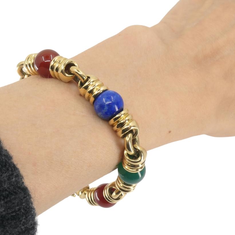 Bracciale vintage di Bulgari in oro 18 carati con pietre preziose.
Il bracciale alterna perline arrotondate e maglie d'oro geometriche che si sentono distintamente Bulgari. Le perle sono di corniola, lapislazzuli e calcedonio verde. Sono distribuiti