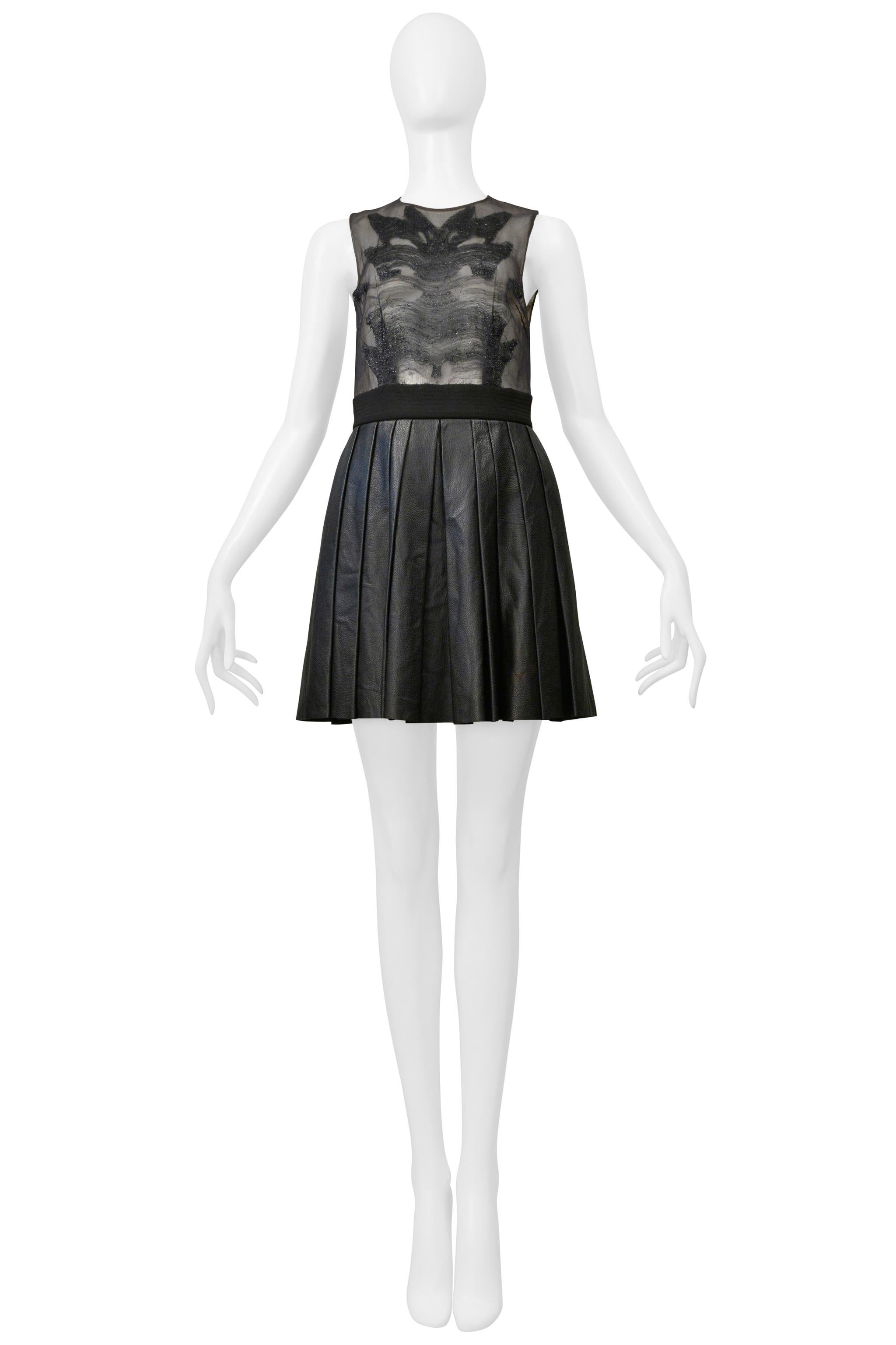 Resurrection Vintage se complace en ofrecer un minivestido negro vintage Byblos con parte superior transparente y falda de cuero plisada. El vestido también presenta un delicado diseño de lúrex metálico en la parte superior de malla, cuello redondo