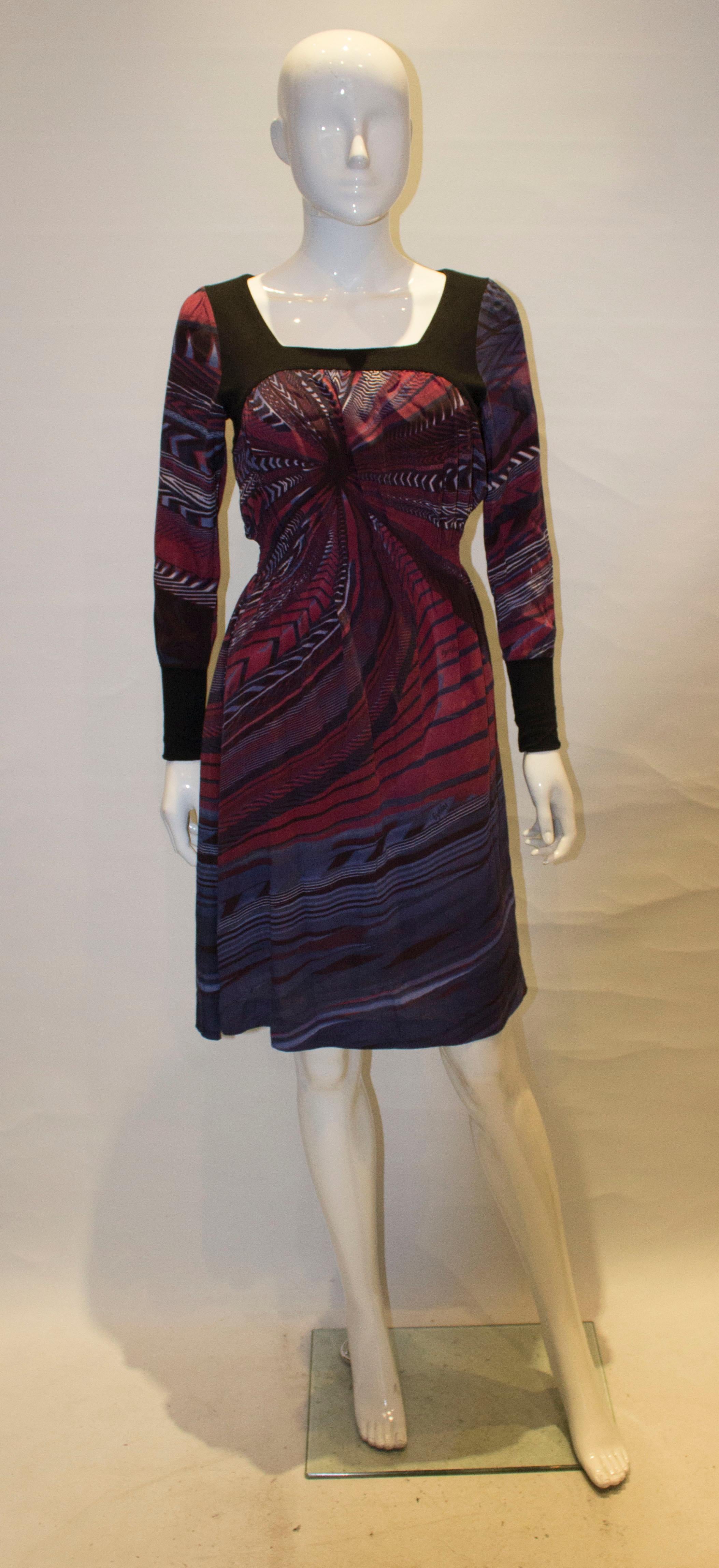 A chic and easy to wear dress by Byblos. The body of the dress is in  a multicolour pink, black and purple print . The dress has elasticated waist with black cuffs and neckline. It is fully lined.