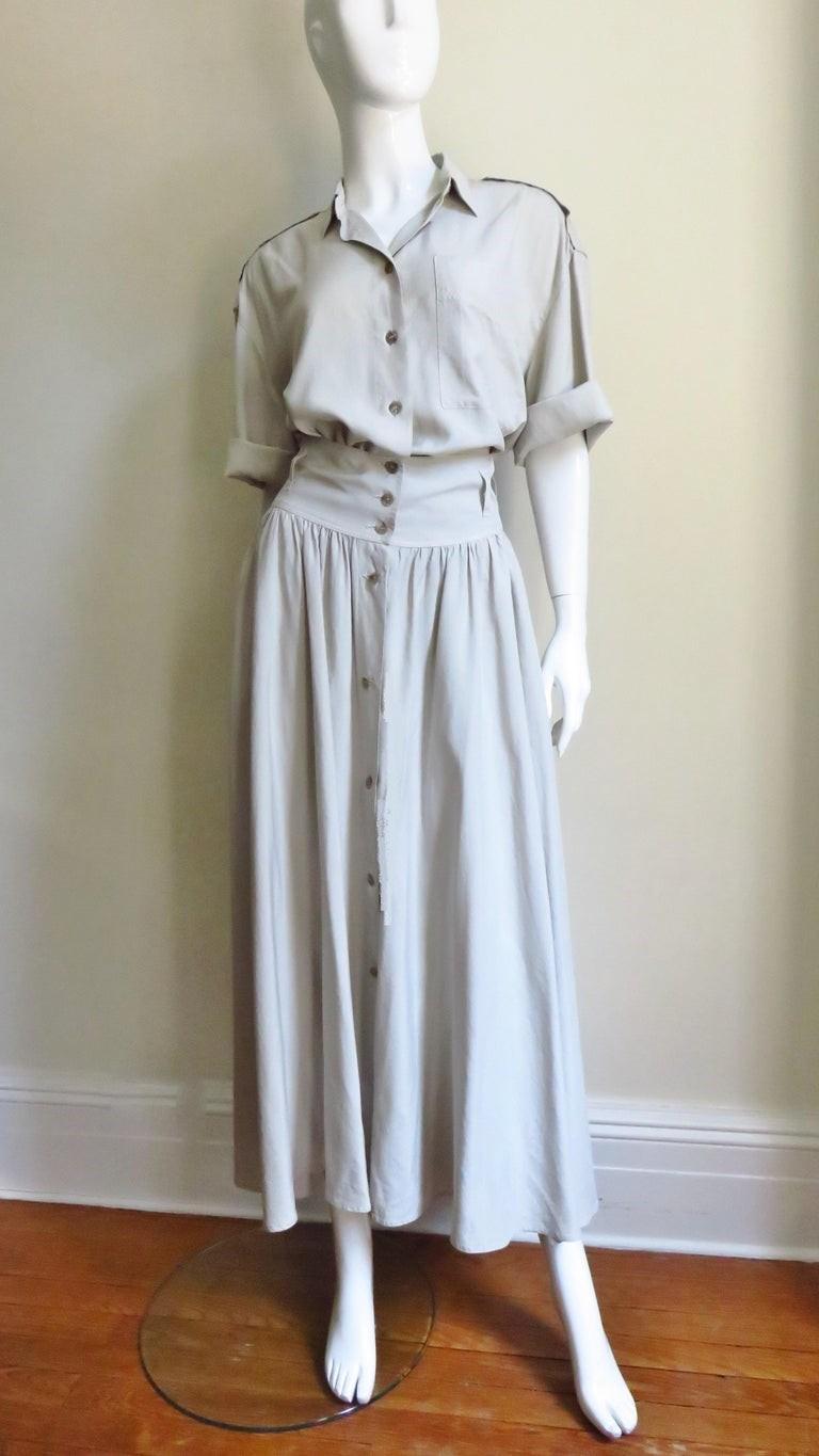 A fabulous set in off white silk from Byblos consisting of a romper and skirt. The romper has a shirt collar, elbow length sleeves, a breast patch pocket, side seam pockets and epaulets on the dropped shoulders. The button front midi length skirt