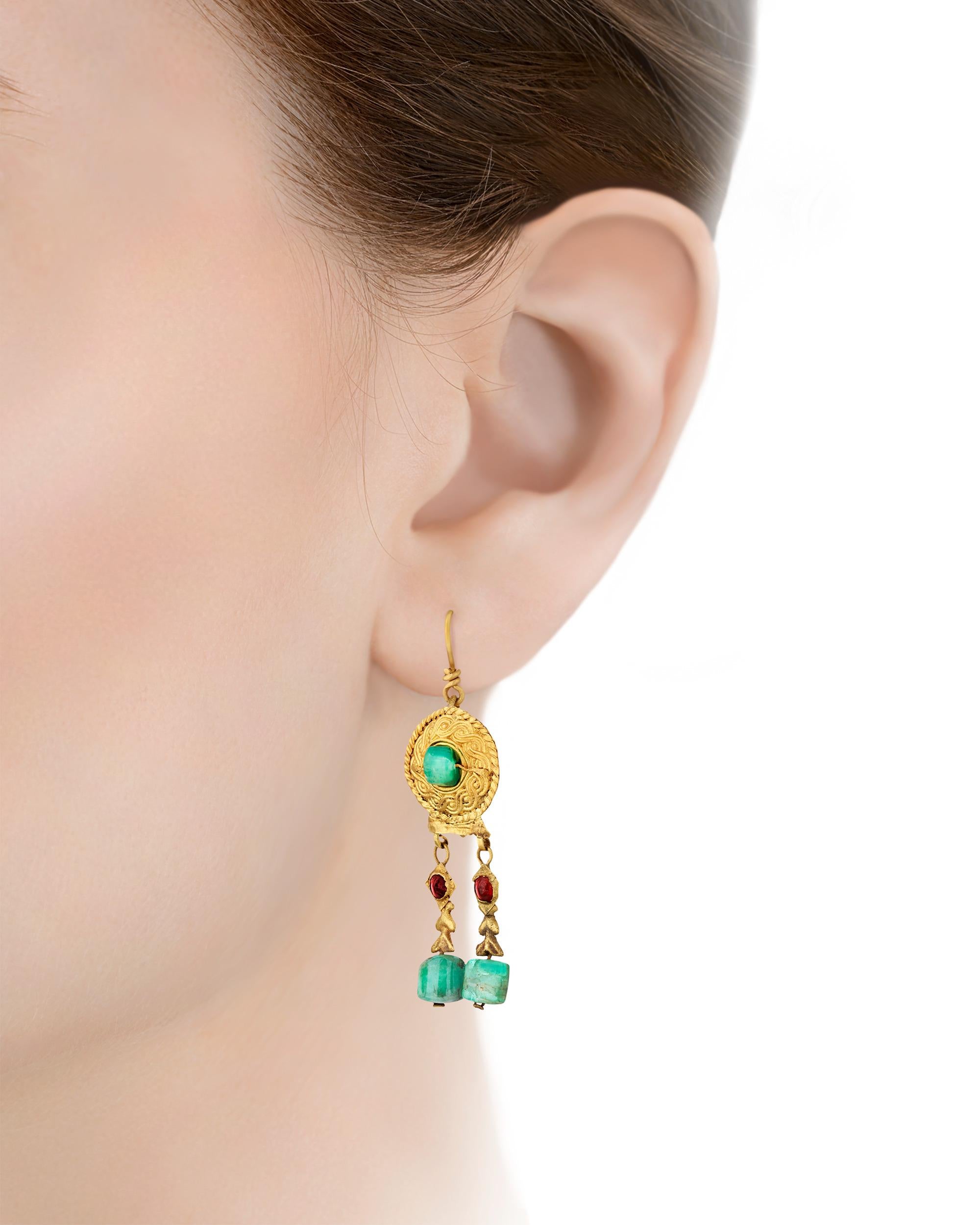 Exuding the grandeur of late antiquity, this pair of garnet and emerald earrings hails from the illustrious Byzantine Empire. The classic drop earrings feature four exquisite green emeralds — one on each shield and two that form the denouement of