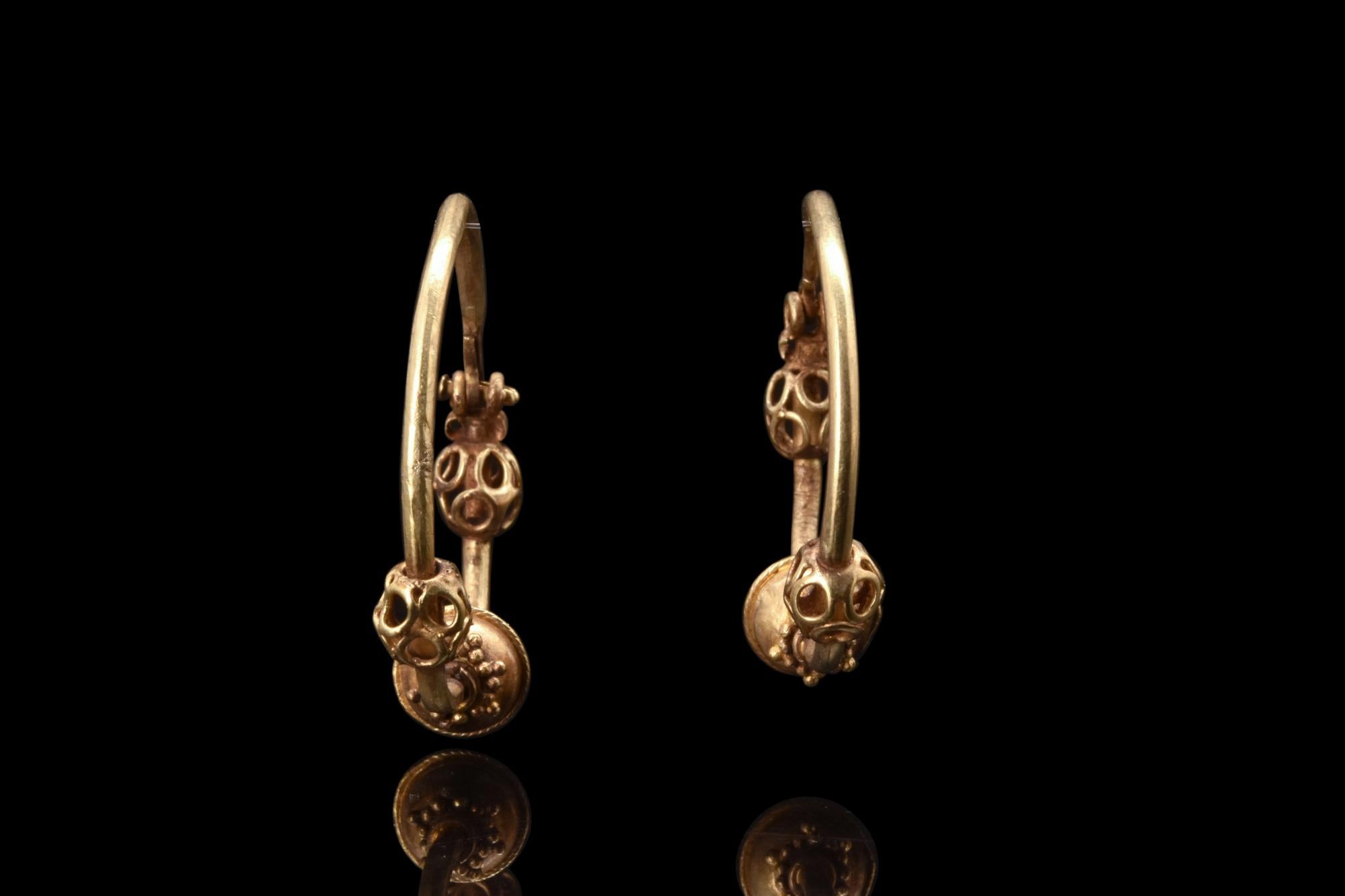 A matched pair of Byzantine gold hoop earrings with a hook and eye closure. These exquisite earrings have three spherical decorative elements suspended along each loop. At the centre, a ball with beading at its edges and at both sides, symmetrical
